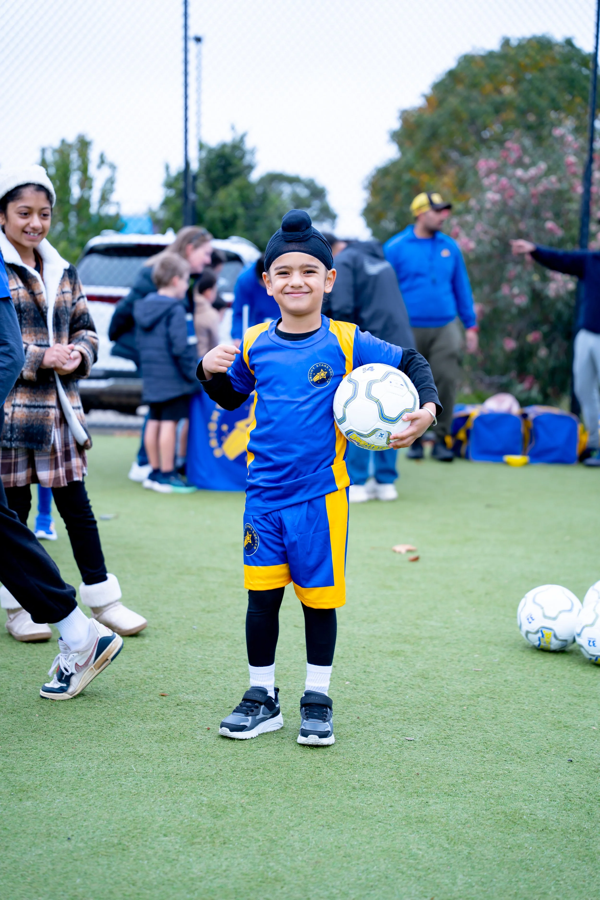 Young boy in Bright Stars Soccer uniform holding a soccer ball on a field with other children and adults in the background.