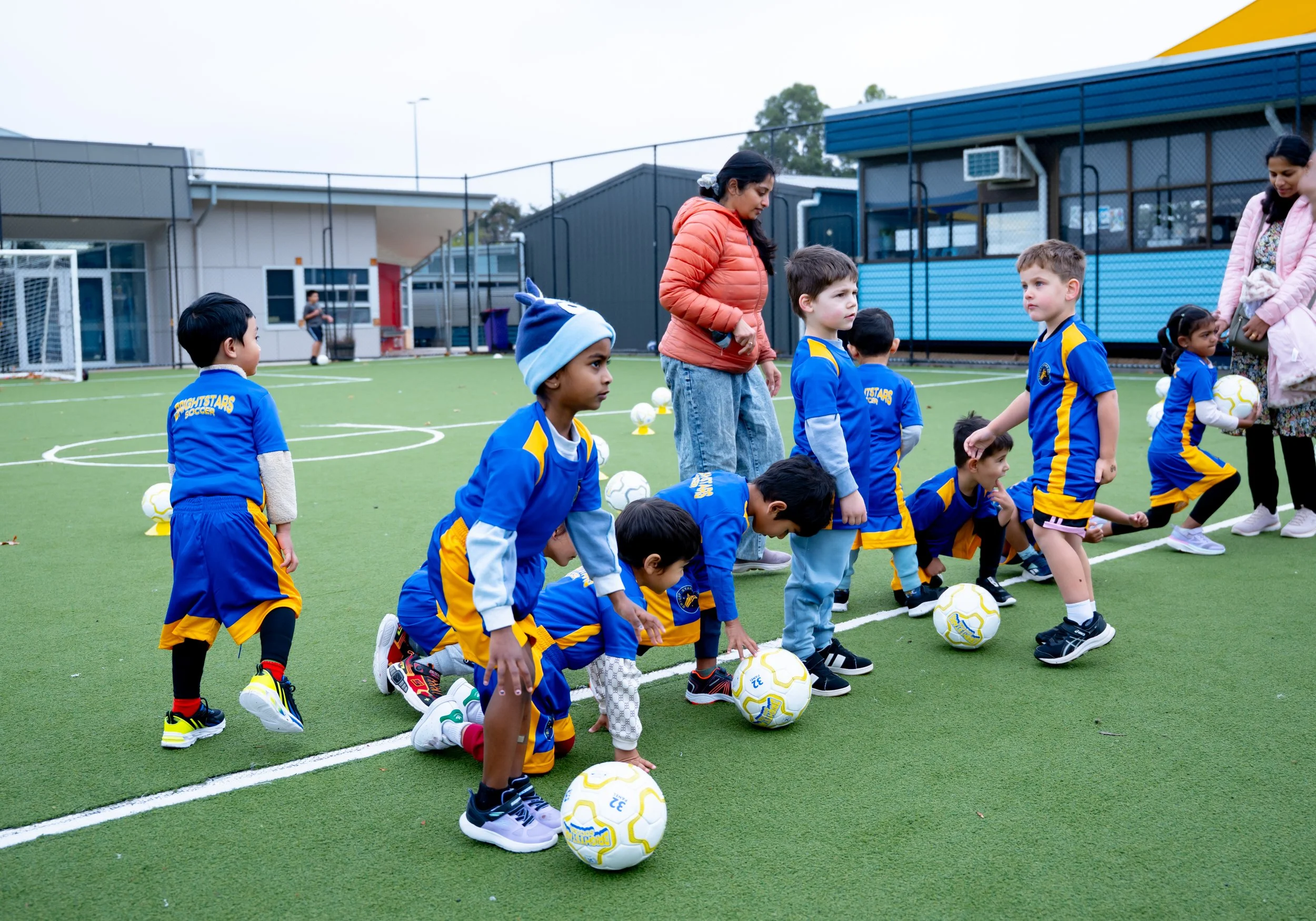 Young children in blue soccer uniforms lined up on an artificial turf field participating in a soccer practice