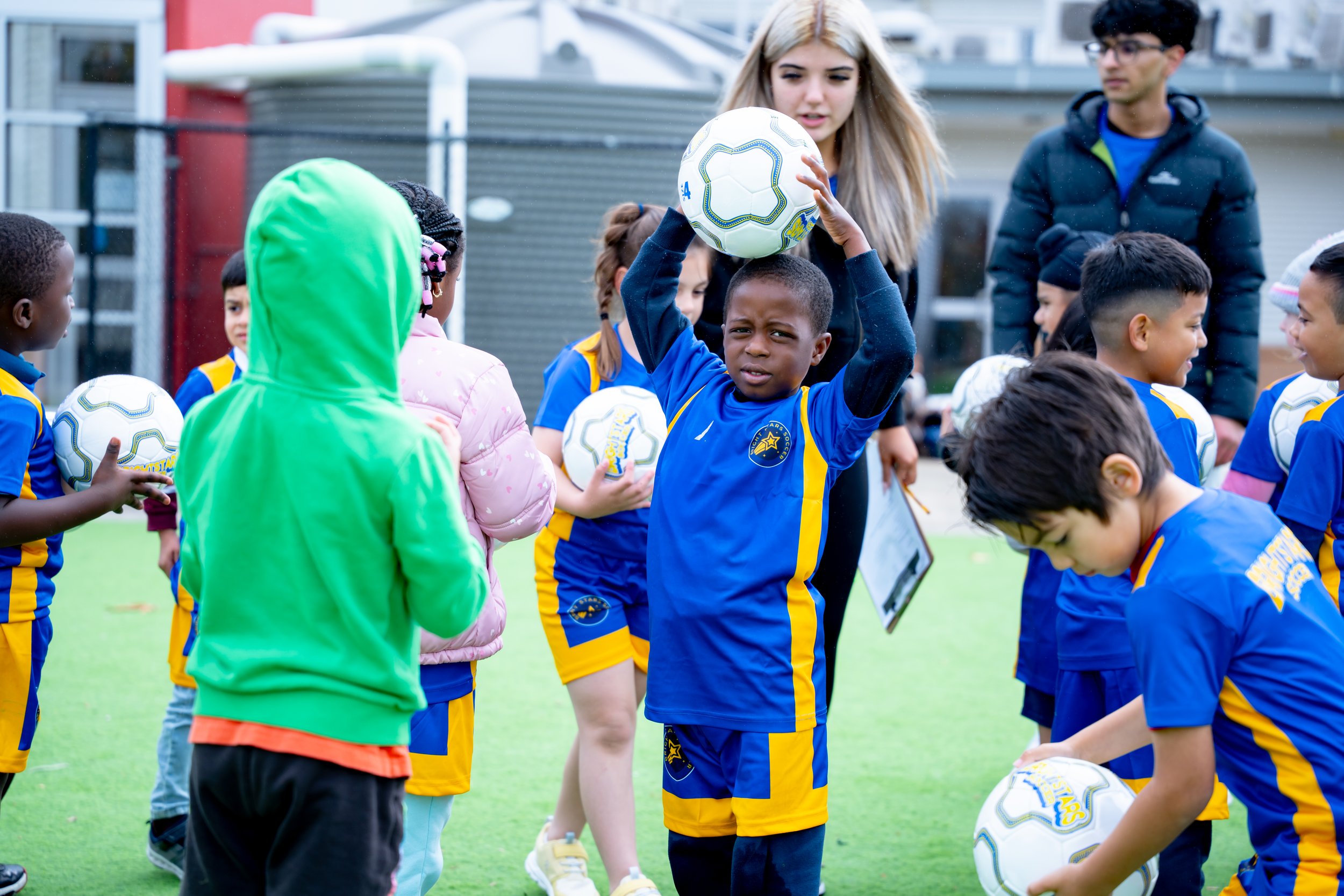 Young children in blue and yellow soccer uniforms gather on a field