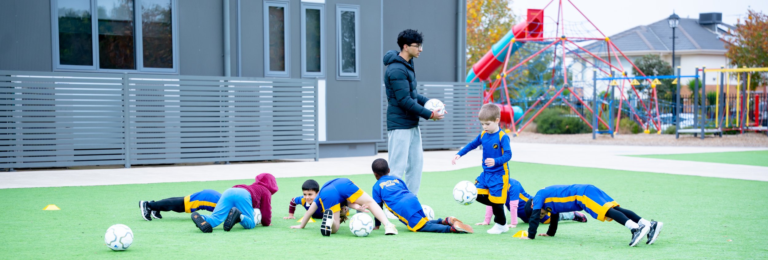 Children practicing soccer drills on a field while a coach instructs and holds a soccer ball