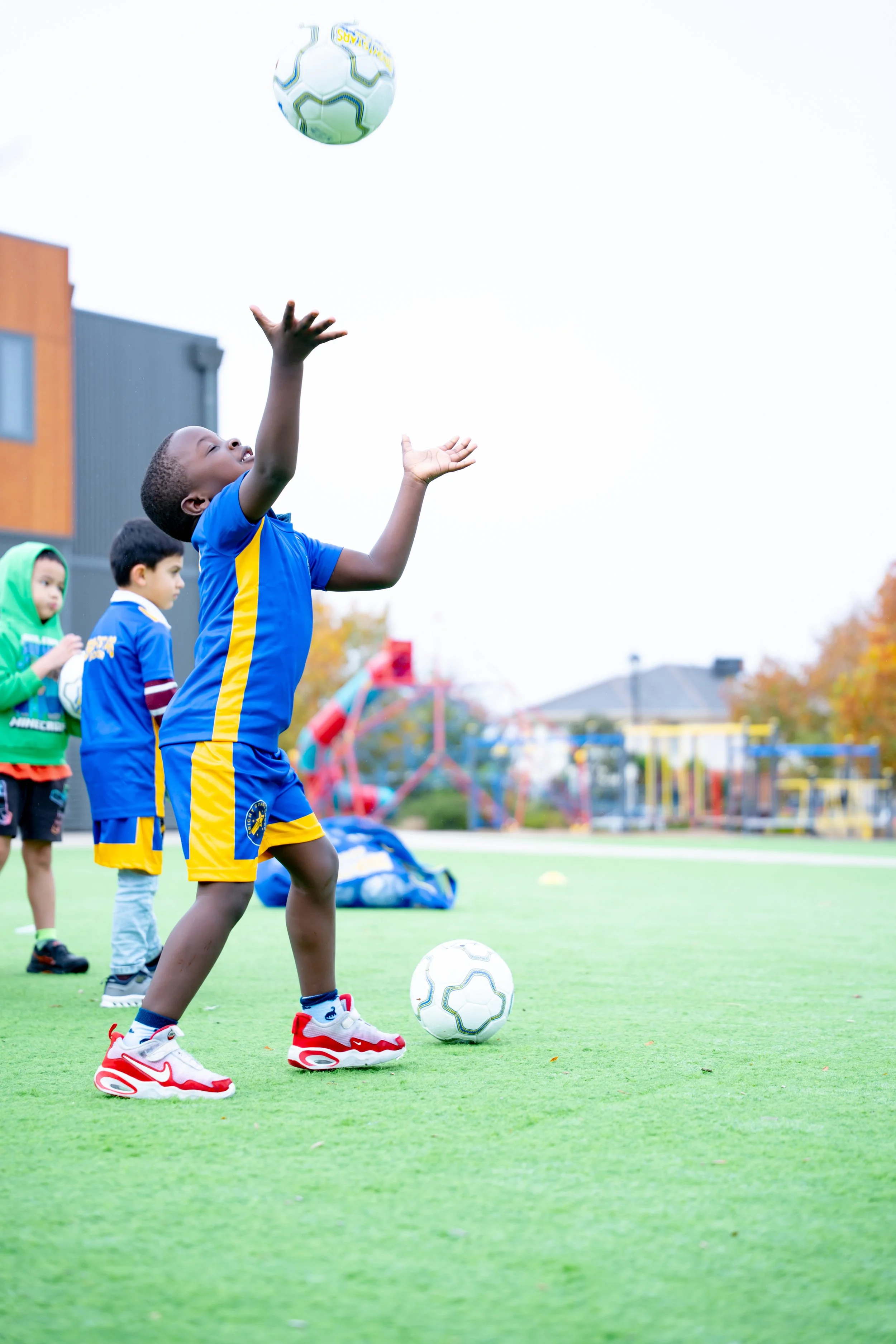 A young boy in a blue and yellow soccer uniform is playing soccer on a green field during daytime. 
