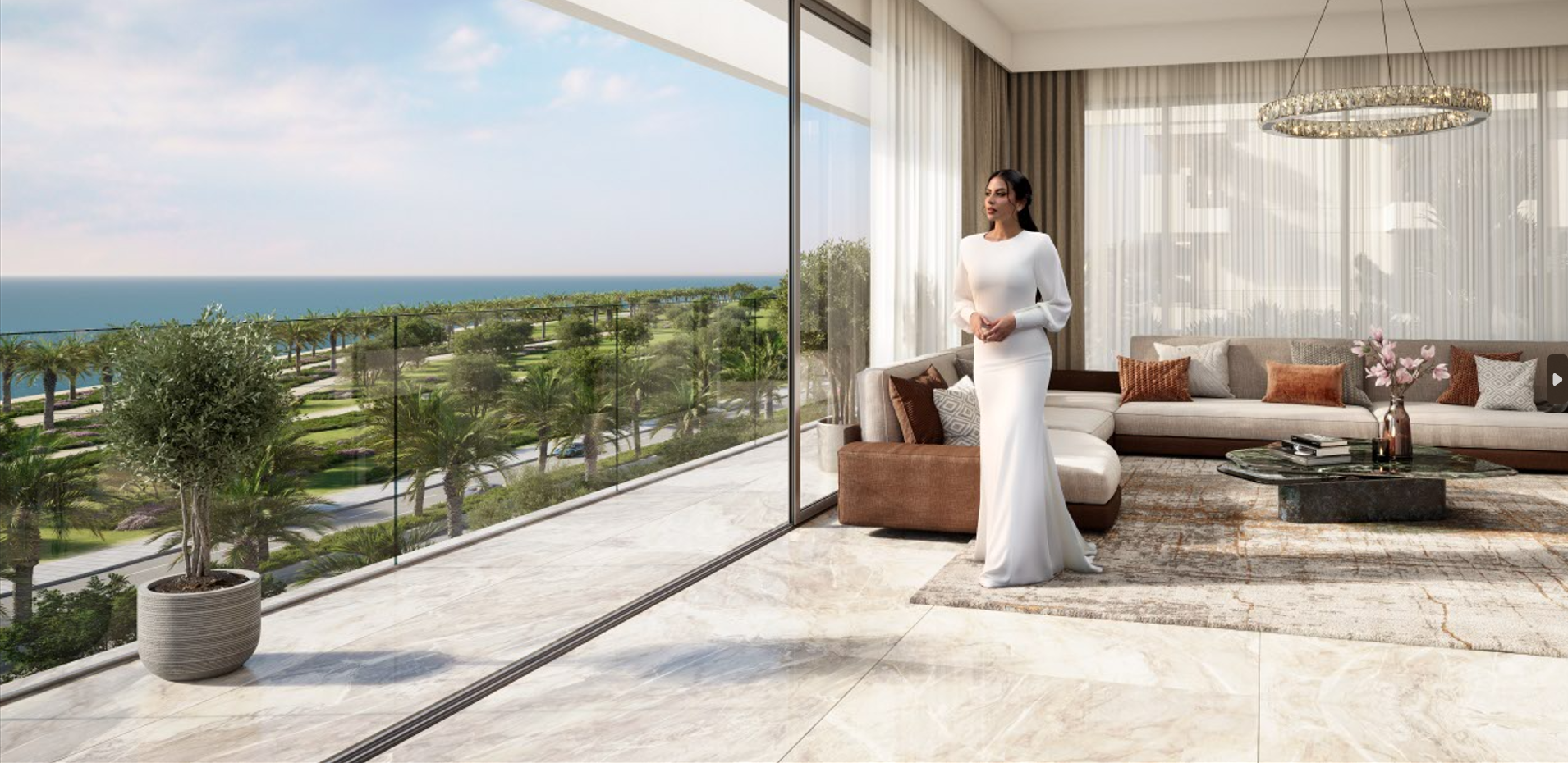 Woman in white dress standing in modern living room with large glass windows overlooking a lush outdoor landscape and ocean
