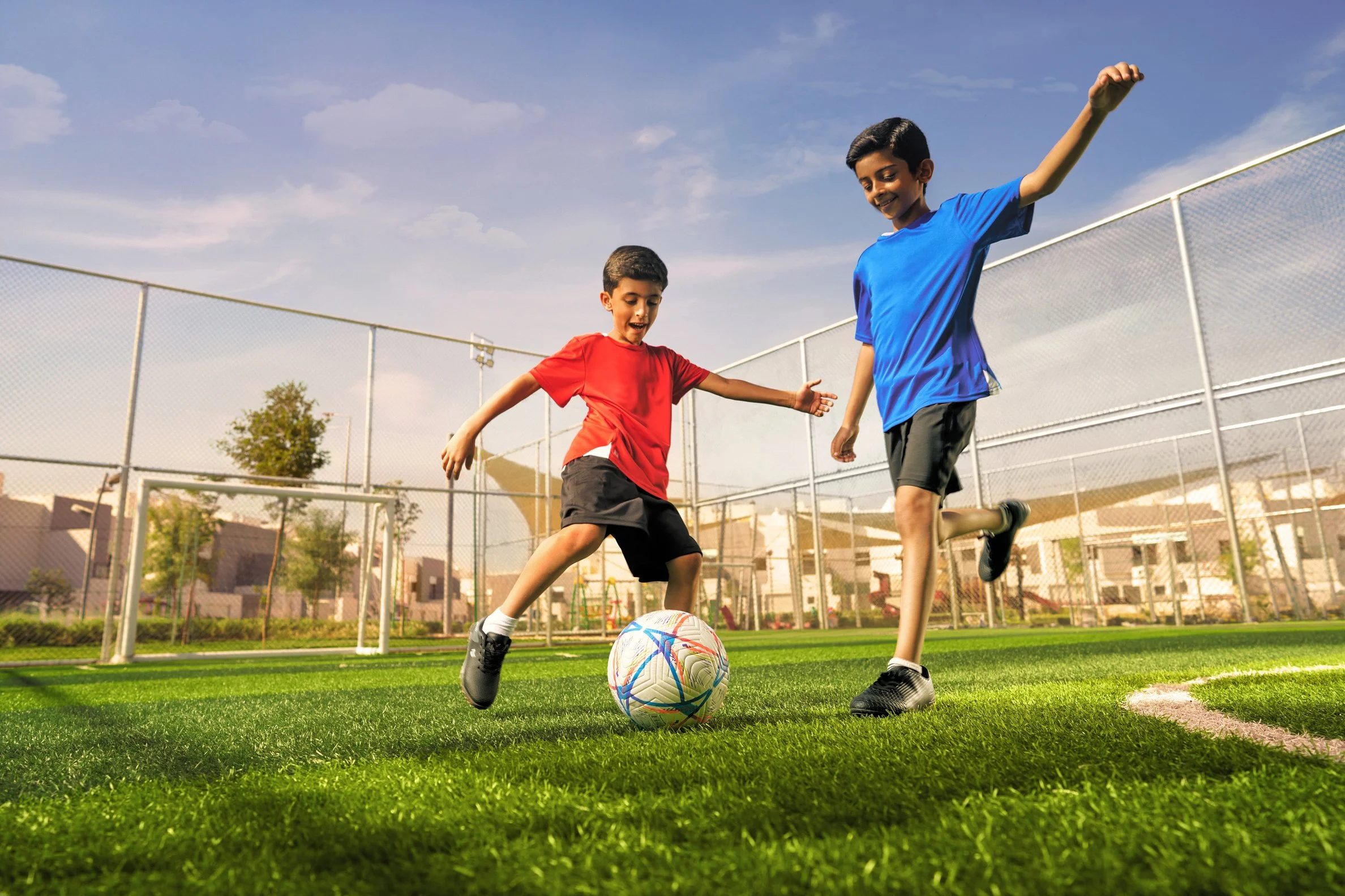 Two boys playing soccer on a field, one in a red shirt and the other in a blue shirt, with a soccer ball between them.