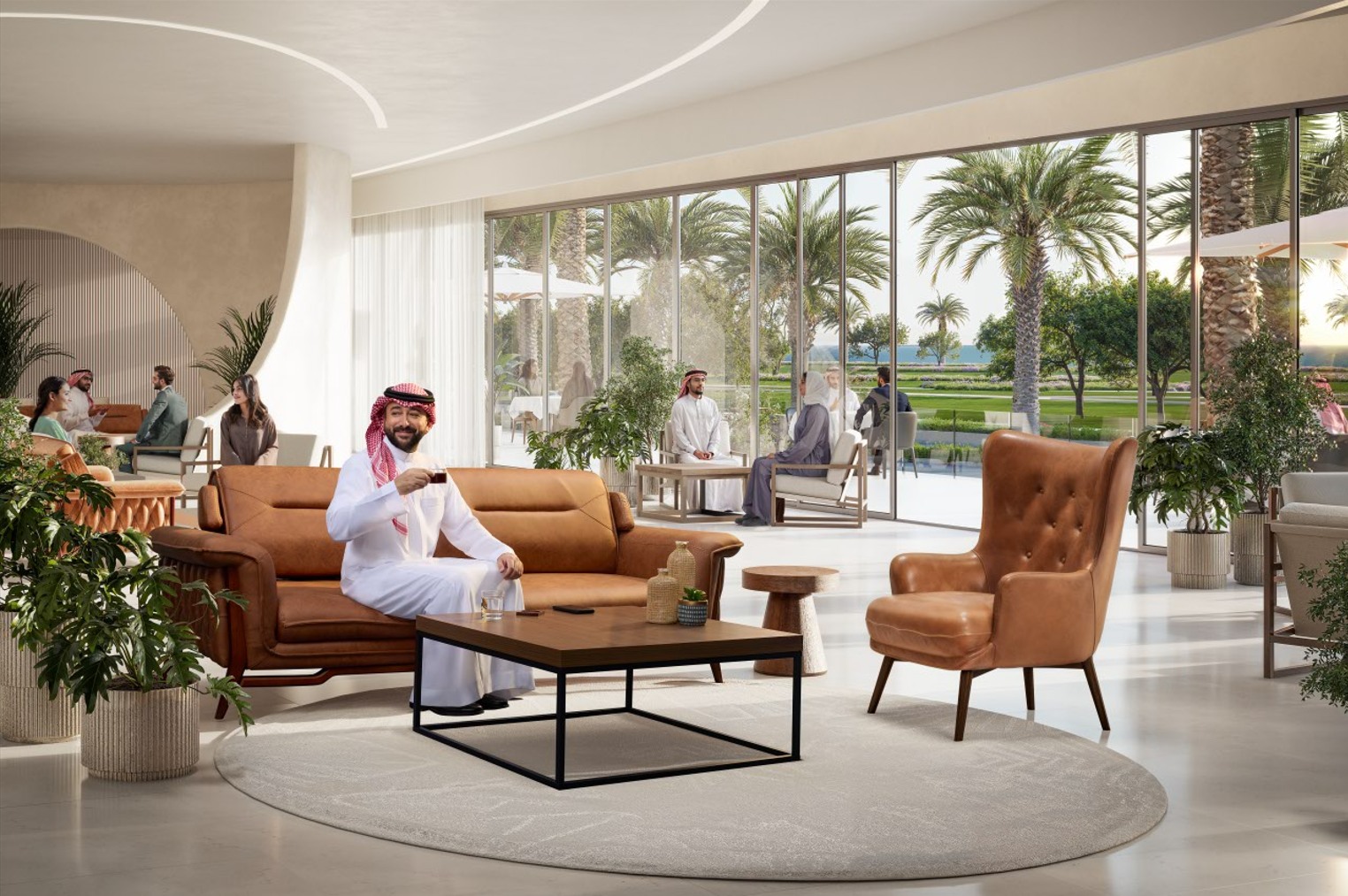 Lobby area with large windows overlooking palm trees and outdoor seating, featuring a man in traditional Middle Eastern attire sitting on a sofa holding a cup, surrounded by modern furniture and green plants.