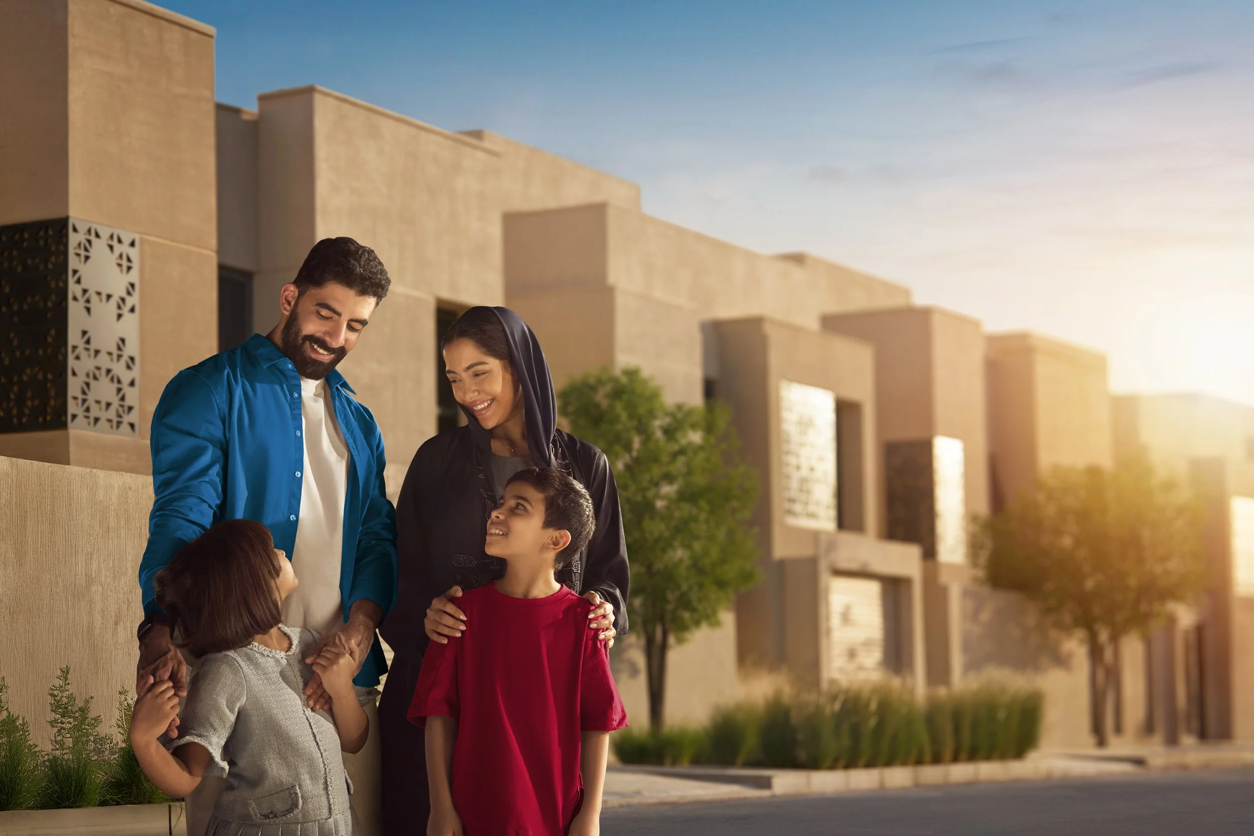 A family with two adults and two children standing outside a modern building, smiling and interacting during sunset.