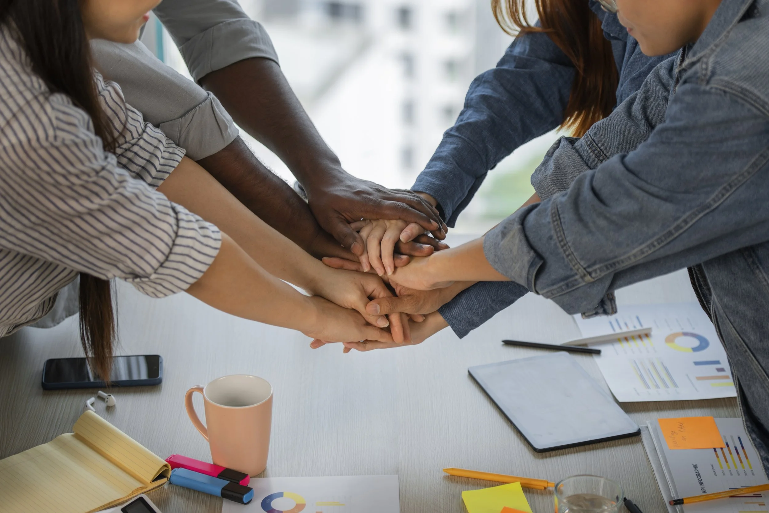 Group of diverse people stacking hands together on a conference table in a meeting room.