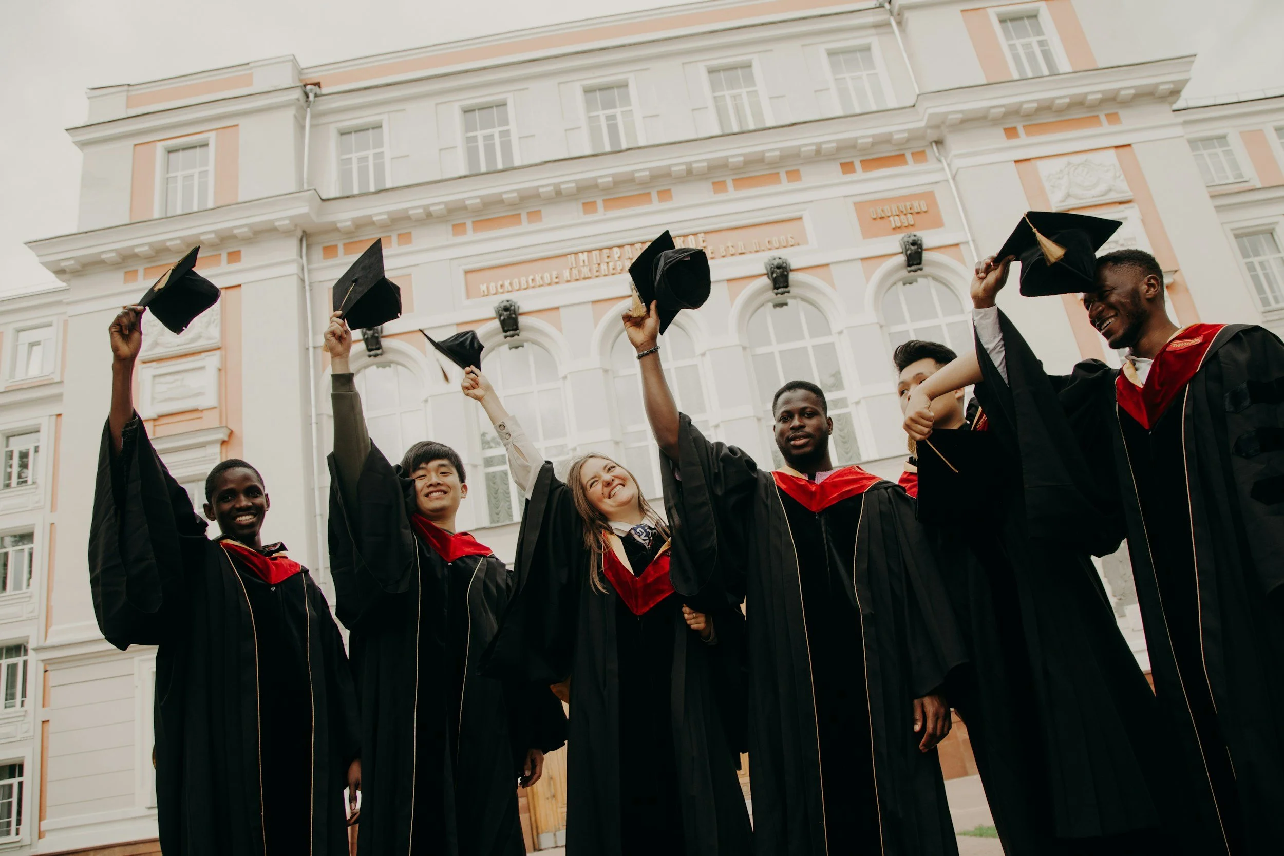 Group of diverse graduates in caps and gowns celebrating graduation outside a historic building.