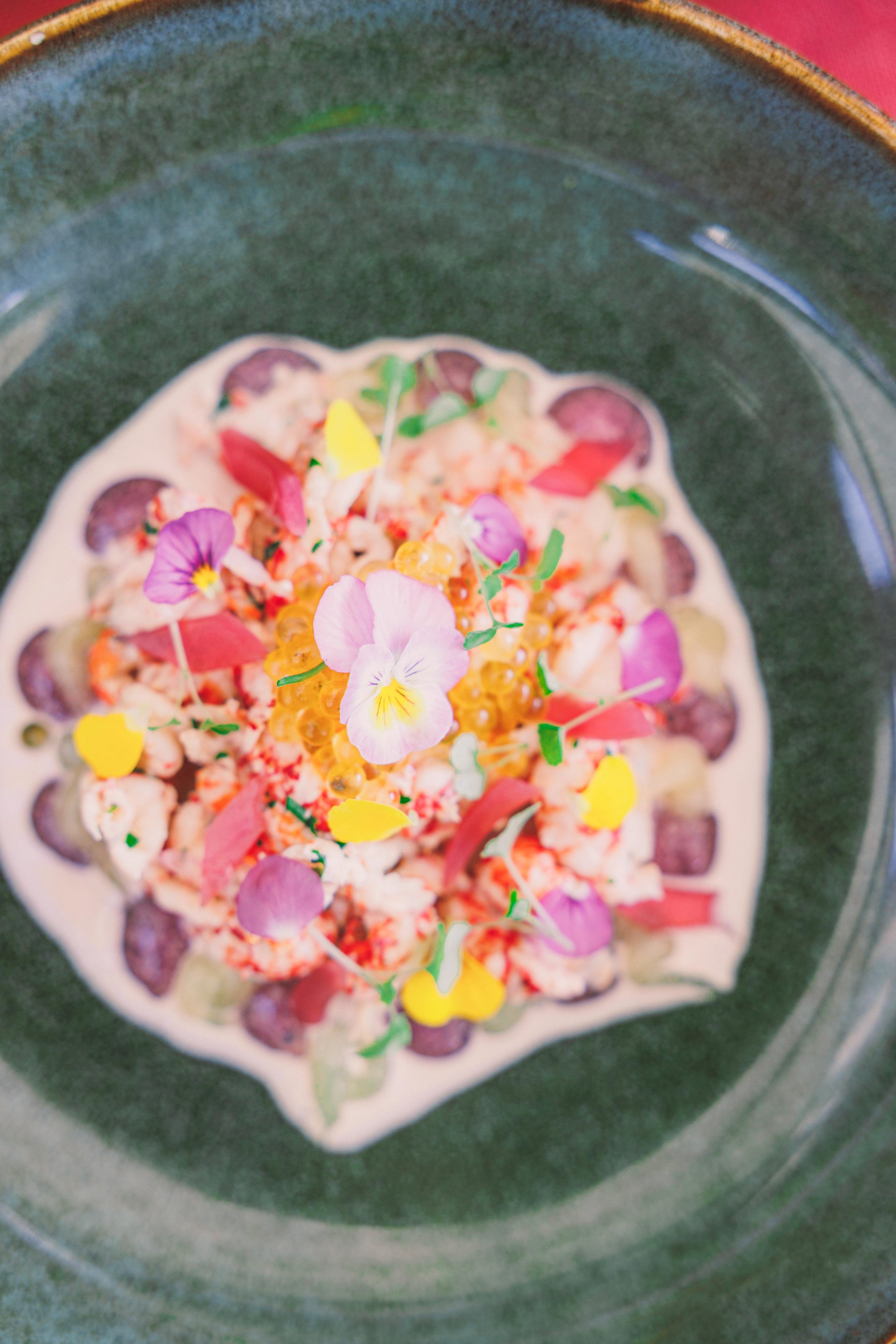 A gourmet dish with seafood and edible flowers on a green plate.