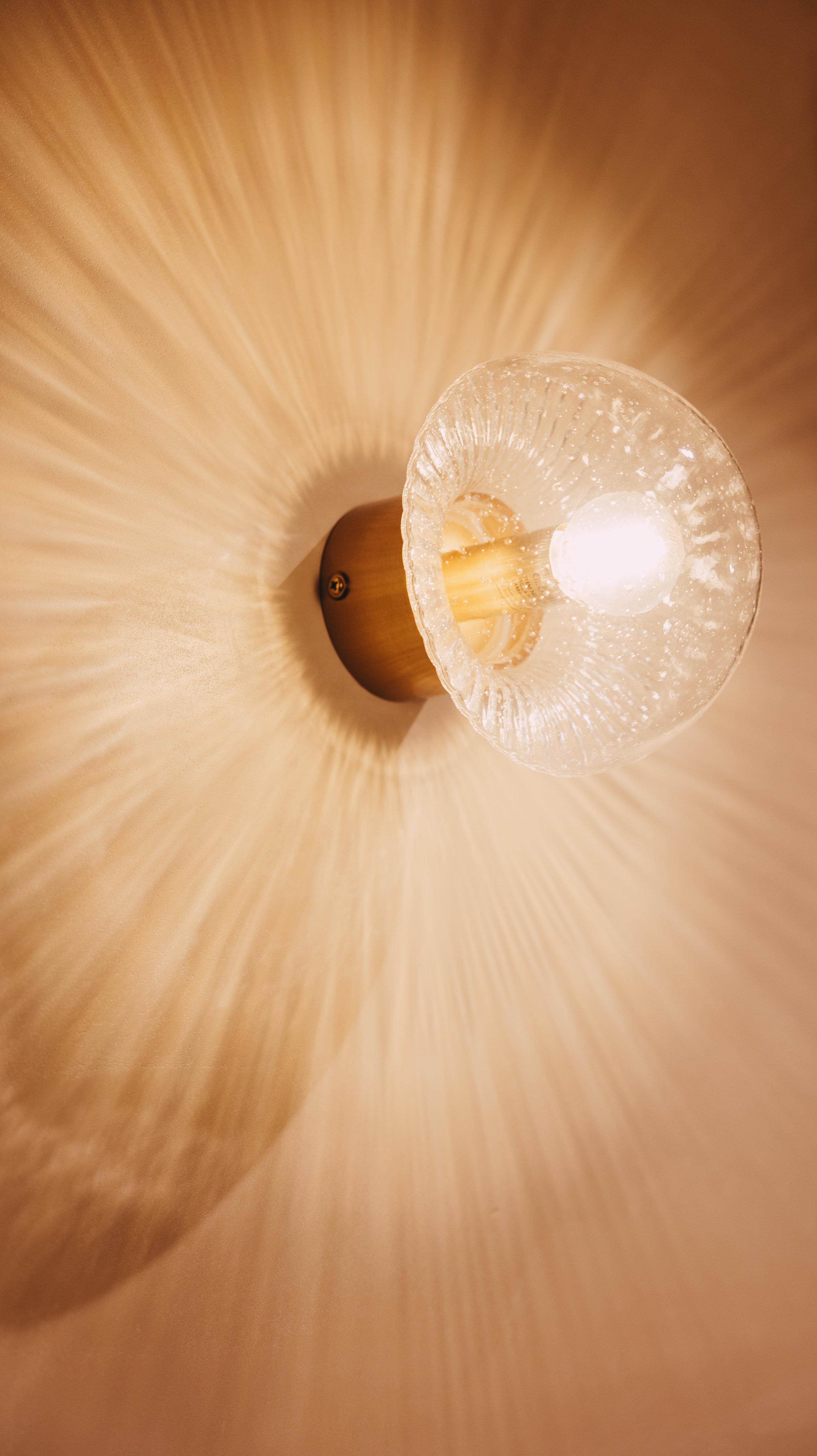 Wall-mounted light fixture with a glass shade and warm glow, casting a radial pattern of light on the wall.