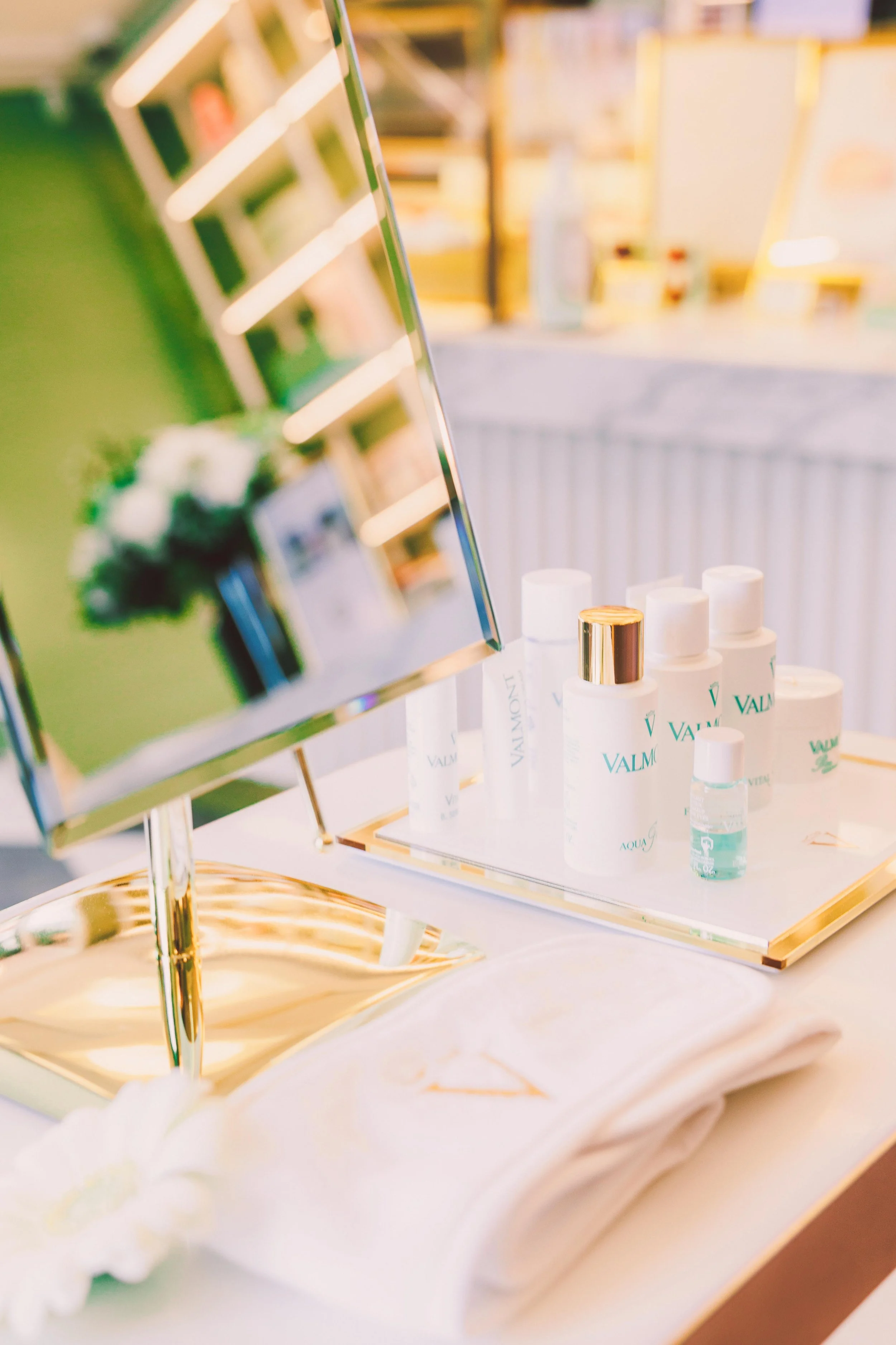 Beauty products, including Valmont skincare bottles, placed on a tray with a mirror and a towel on a counter.
