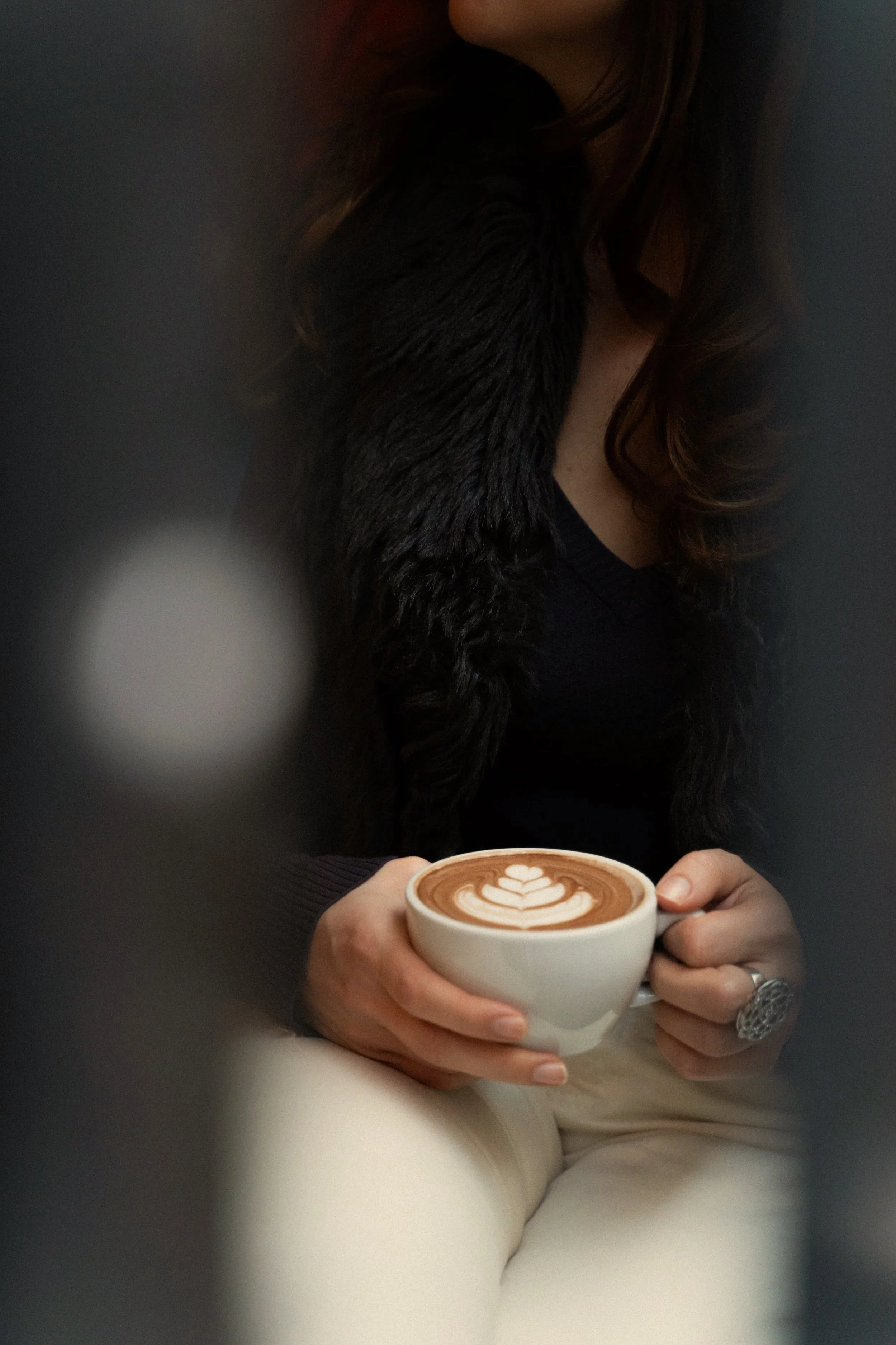 A woman holding a cup of coffee with latte art, sitting indoors.