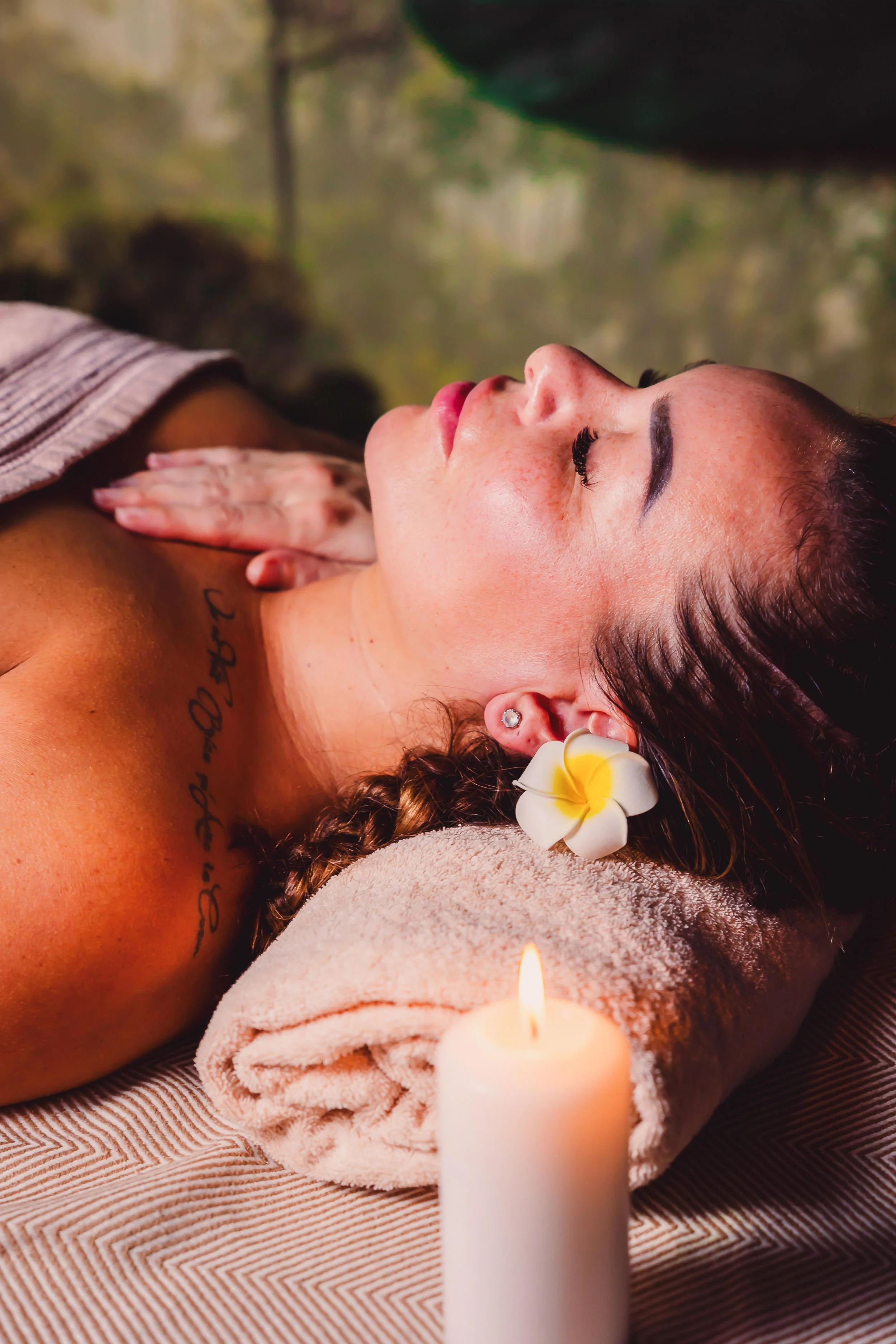 A woman receiving a massage in a spa, with her eyes closed, a flower in her hair, and a candle nearby.