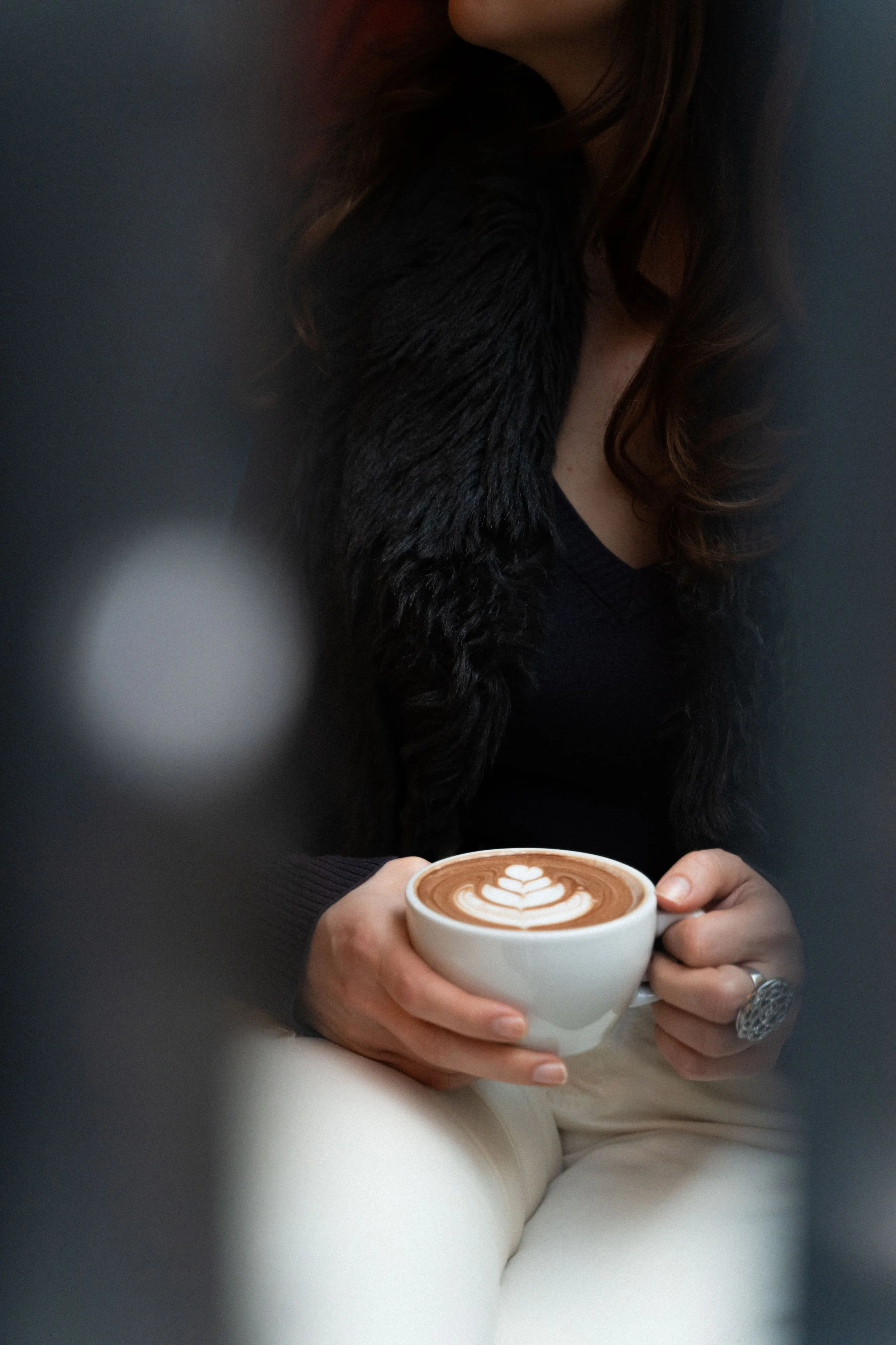 A woman holding a white cup of coffee with latte art, seated in a relaxed setting.