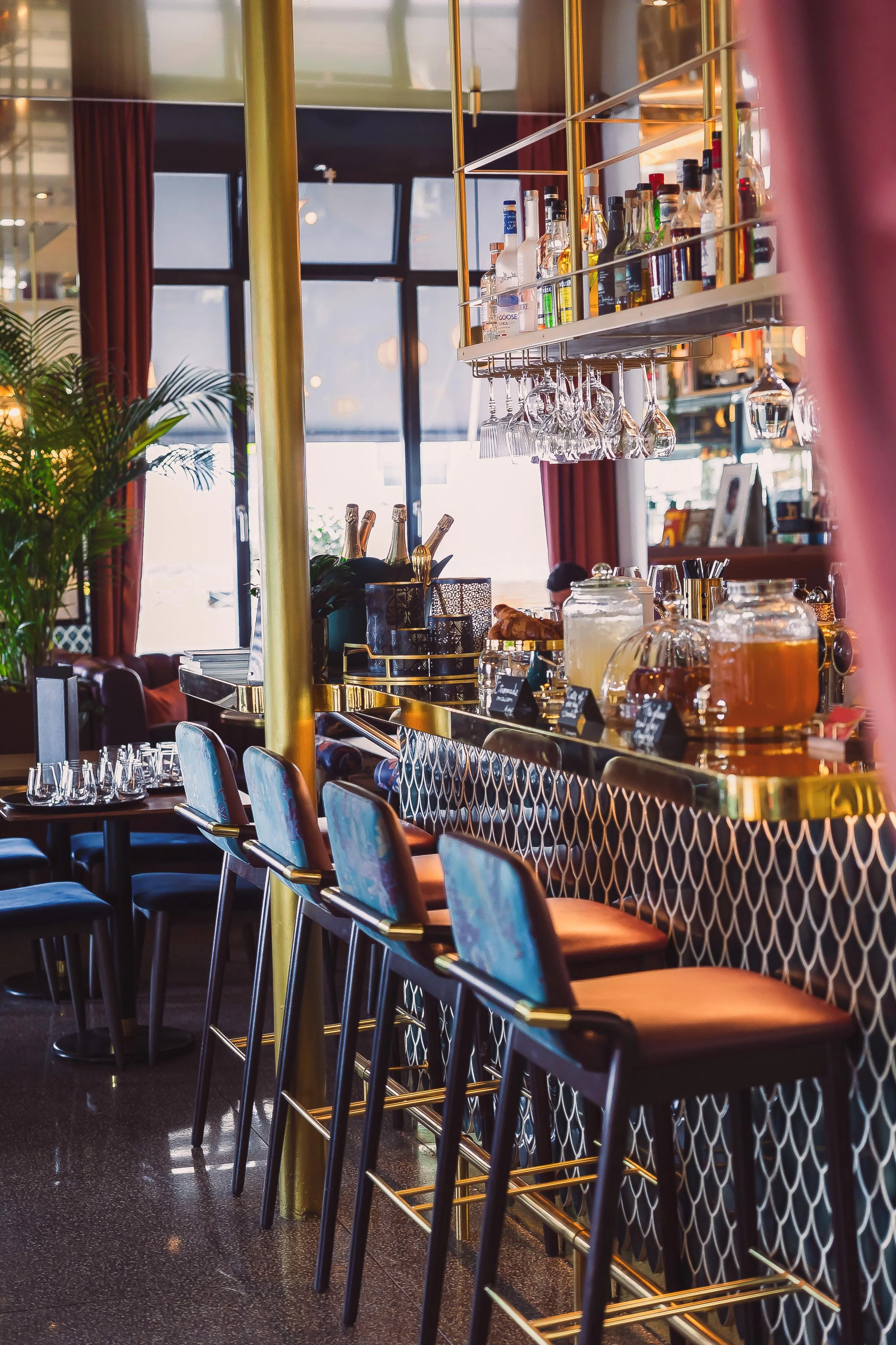 Interior of a upscale bar or restaurant with a bar counter, glassware, bottles of alcohol, and modern decor.