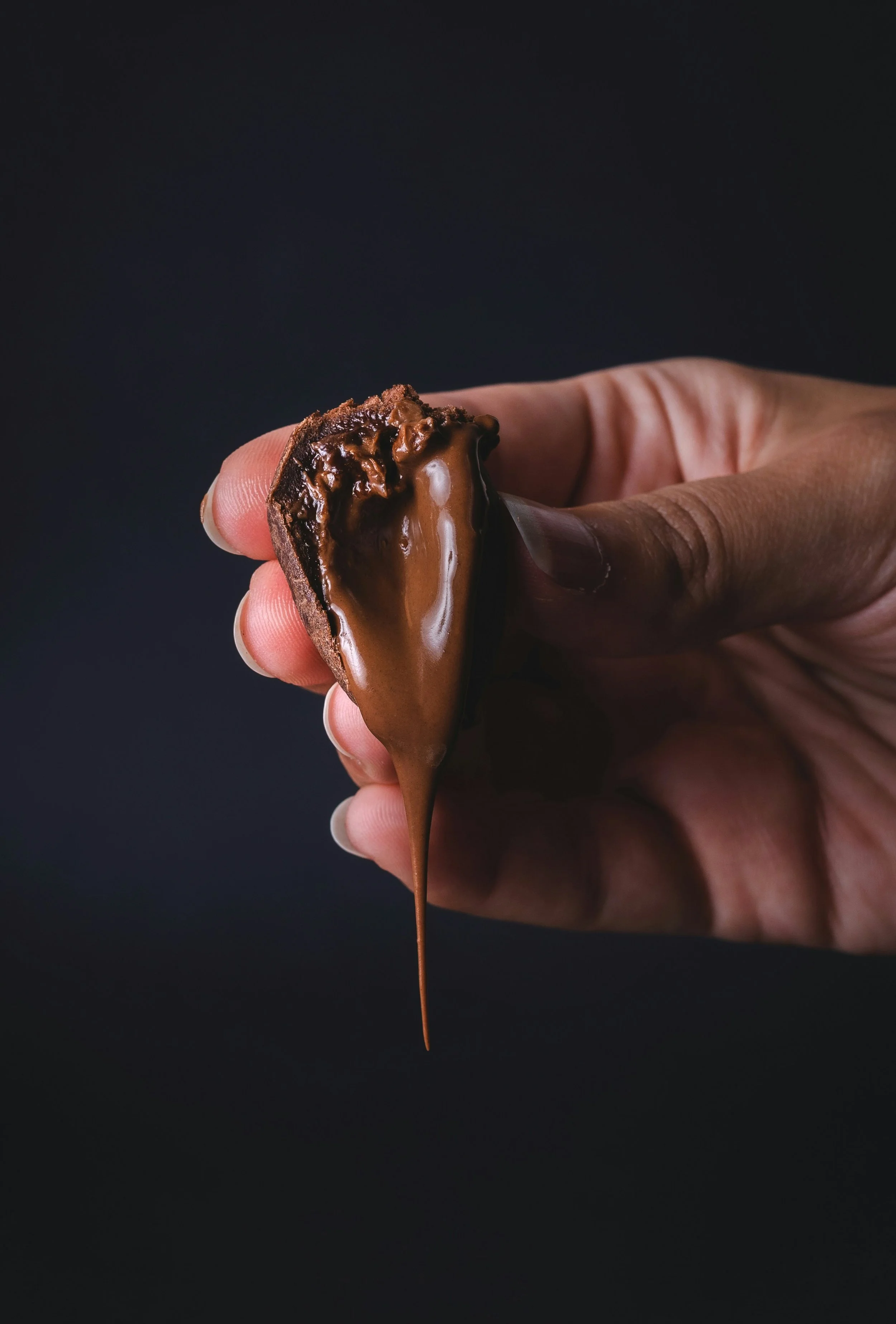 A hand holding a chocolate-covered dessert with melted chocolate dripping down.