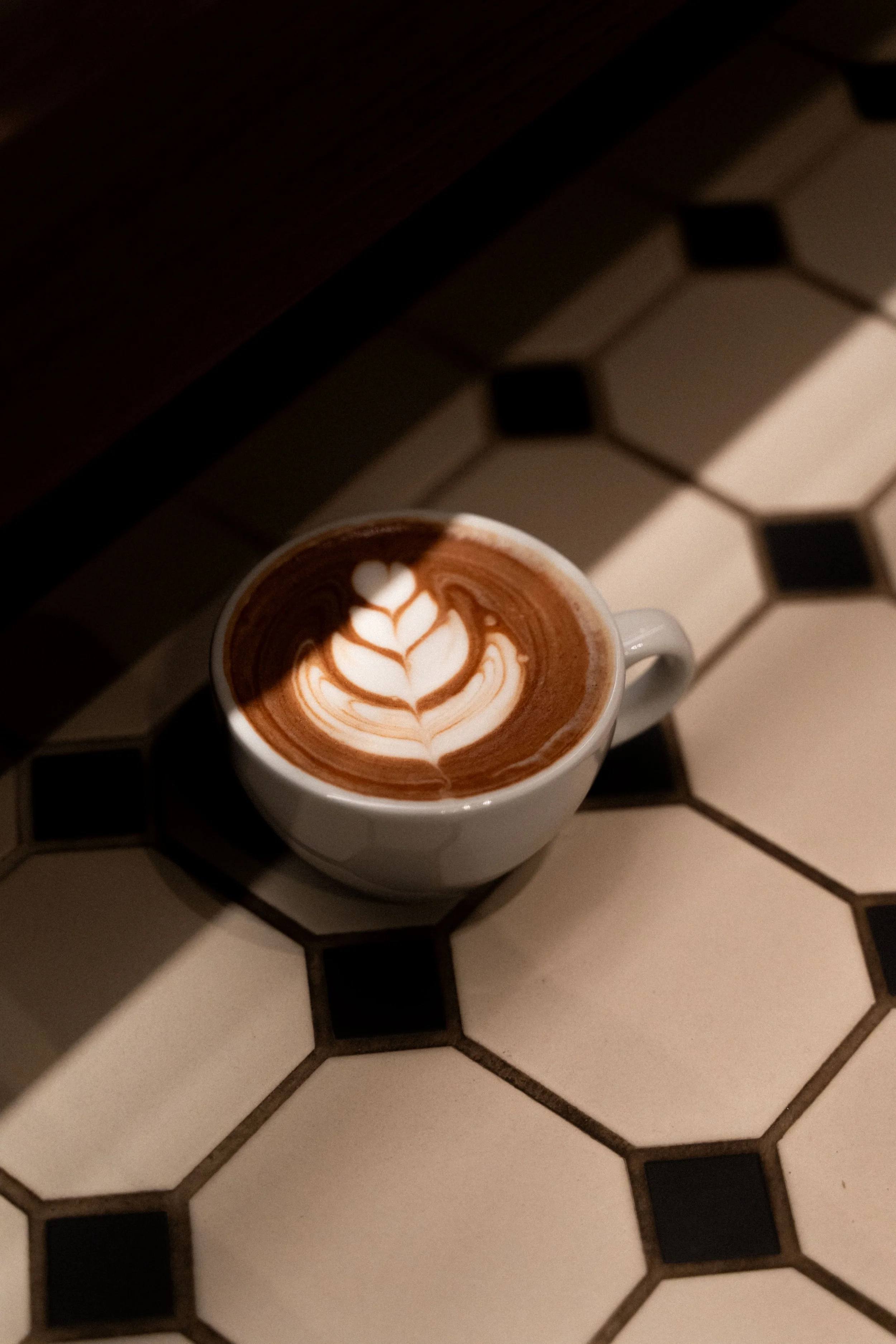 A cup of hot chocolate with latte art on a tiled table with black and white hexagonal tiles.