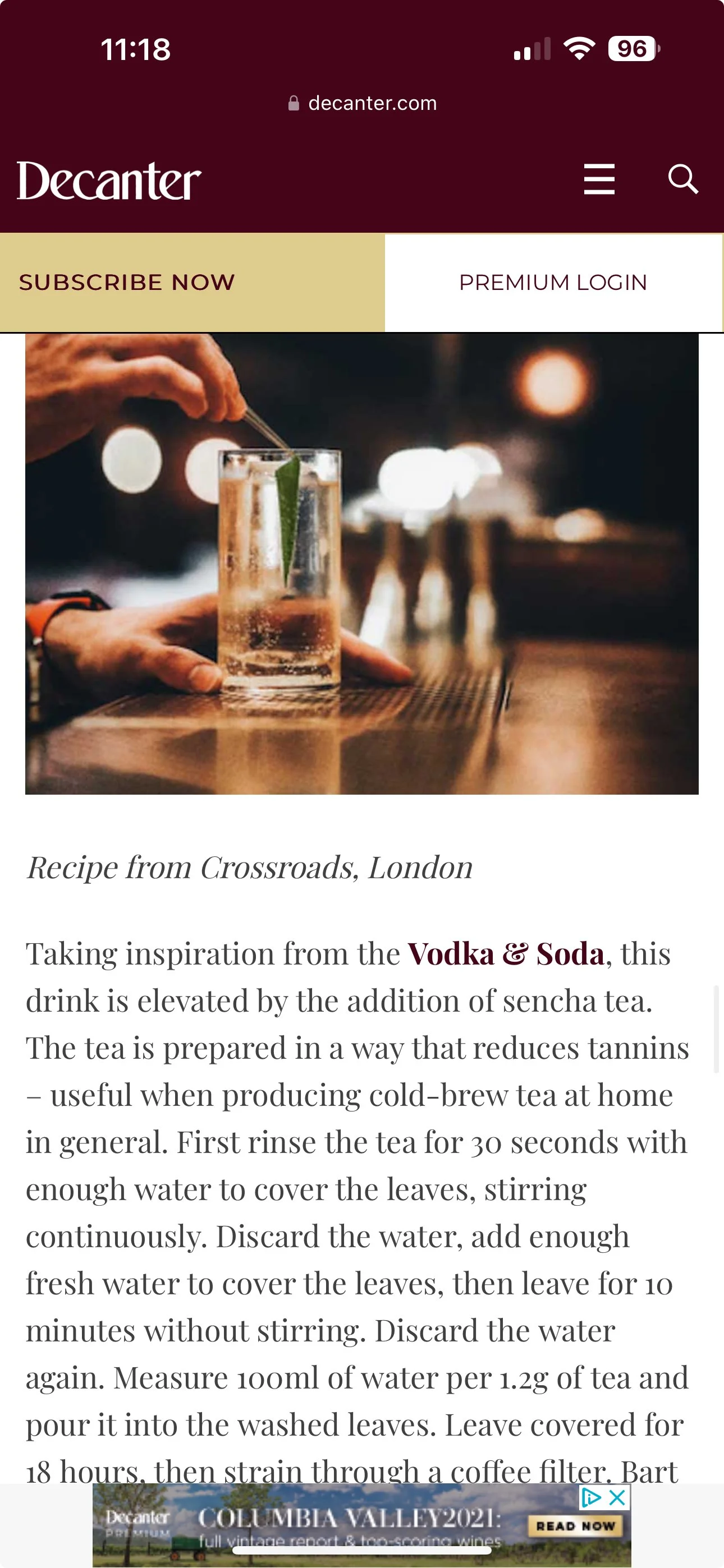 A person preparing a cocktail in a bar, with a glass containing a beverage, a straw, and a green garnish, in a dimly lit environment with bokeh lighting in the background.