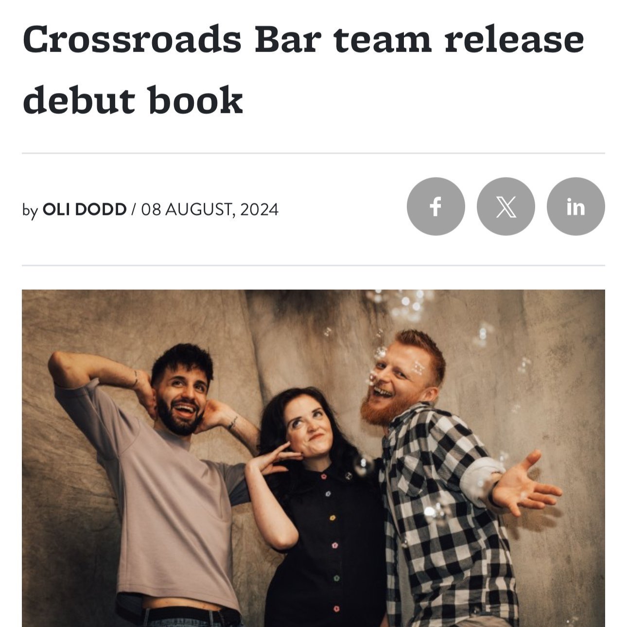 Three people enjoying a party with bubbles and a gray background, smiling and striking playful poses.