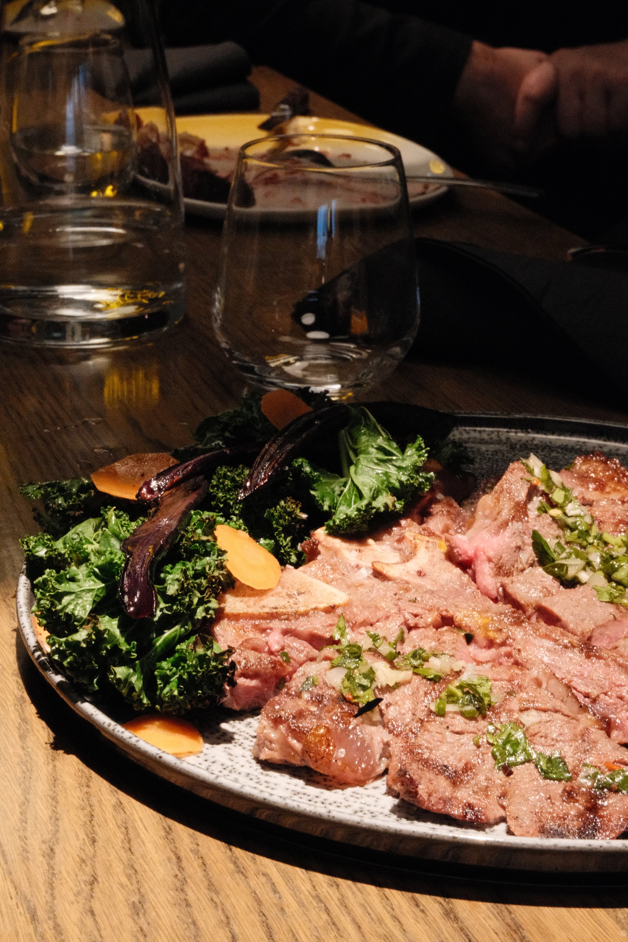 Tallerken med grillet kjøtt og grønnsaker, vann, og glass på et trebord.