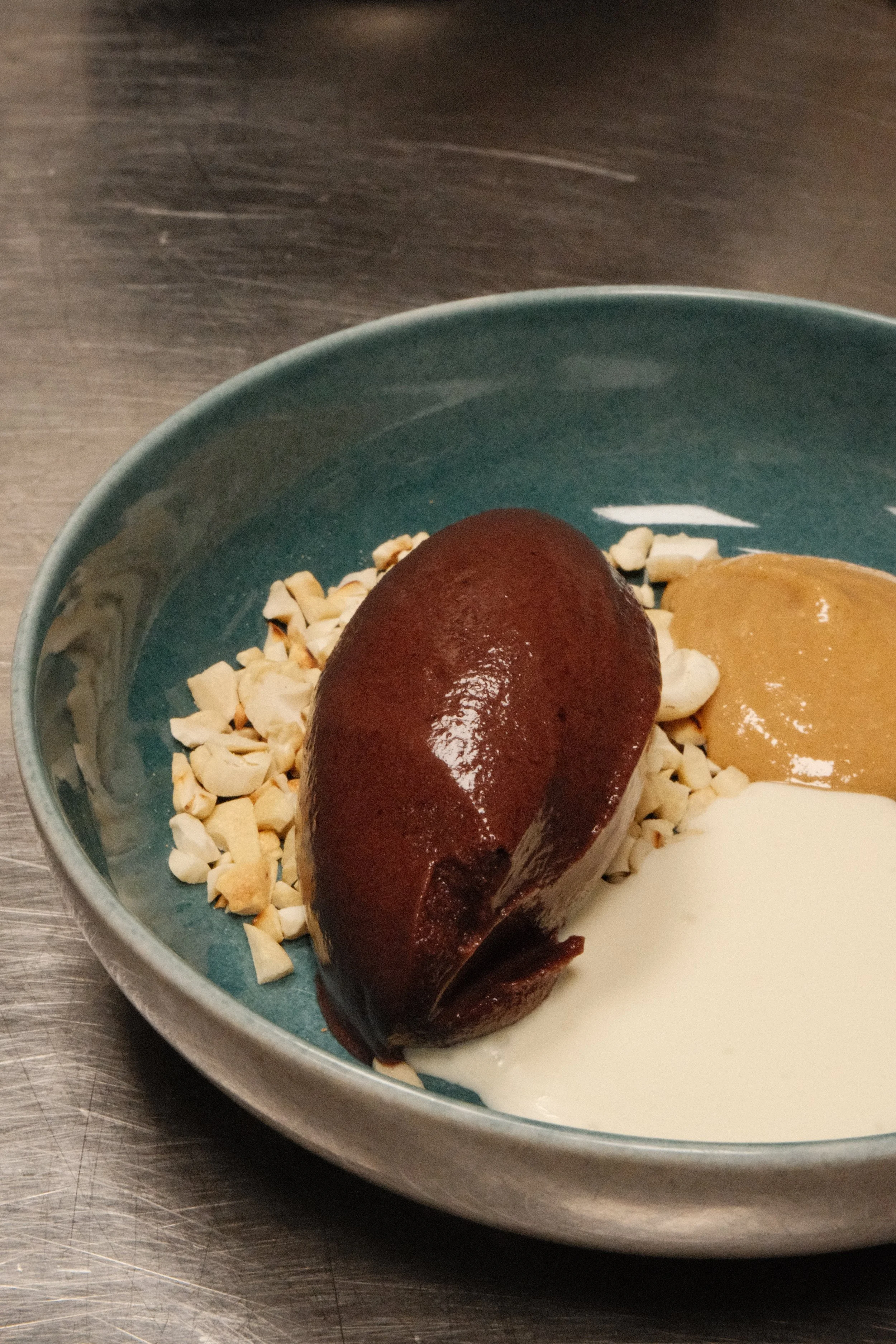 En goddeling med nøtter, karamell, og to typer saus, en av dem er hvit, i en blå tallerken.