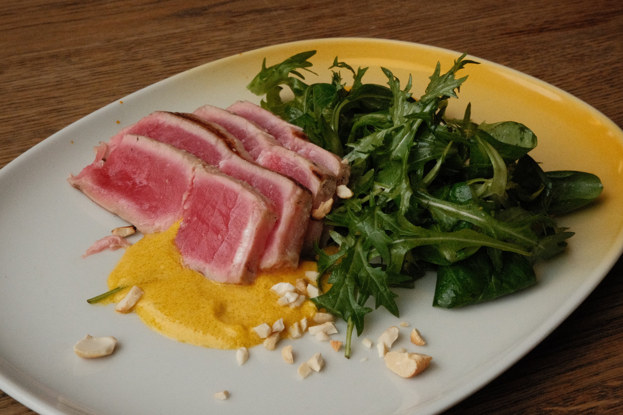 Tungt tunfisk med grønn salat på en hvit og gul oval tallerken.