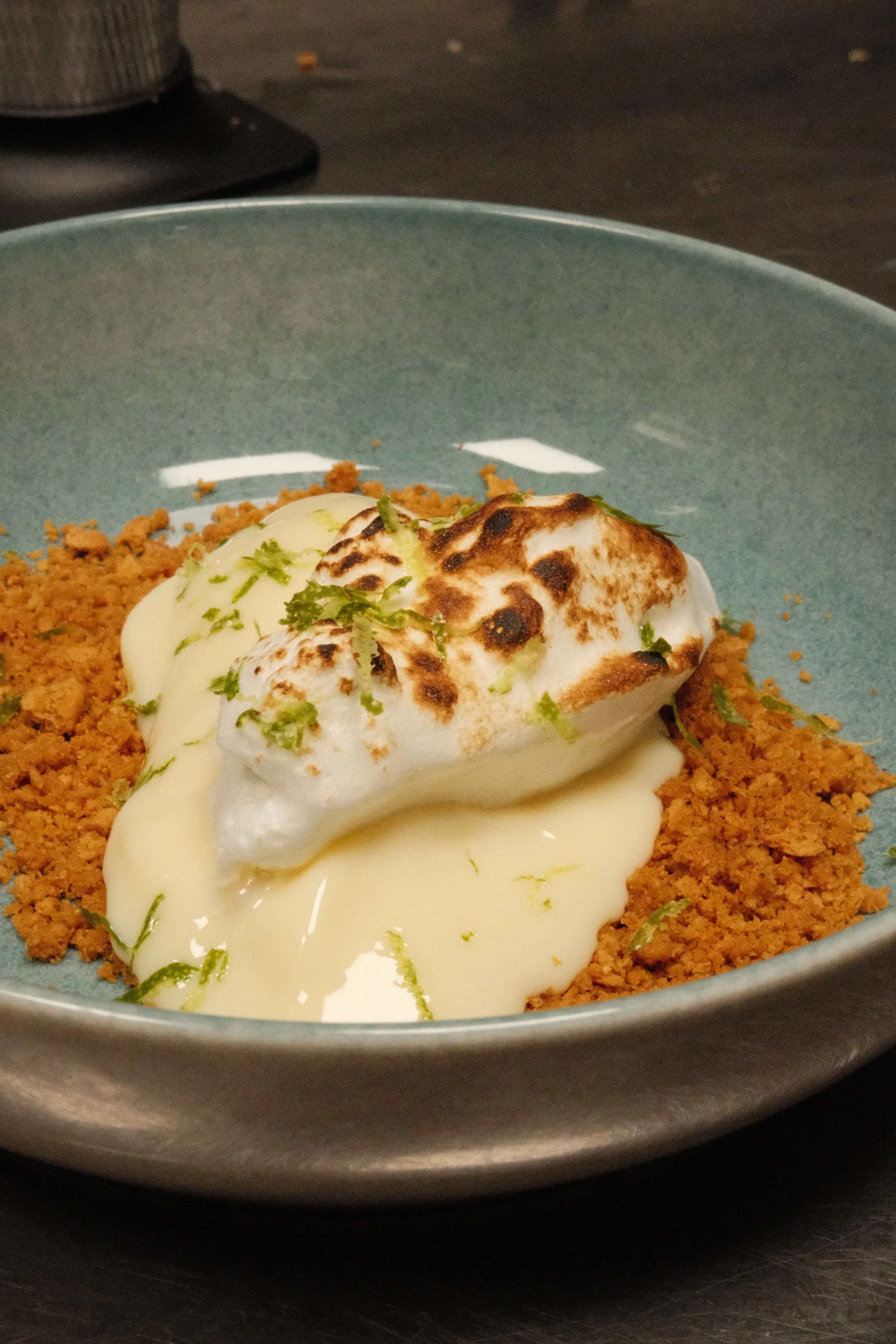 En tallerken med tærtebunn, fylt med kremost, toppet med en brent marshmallow, pyntet med sitronzest.