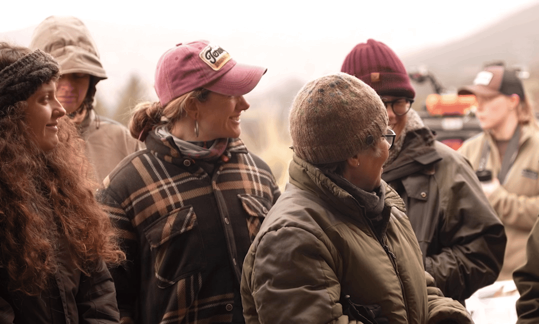 Group of women outdoors in cold weather wearing hats and jackets, smiling and talking.