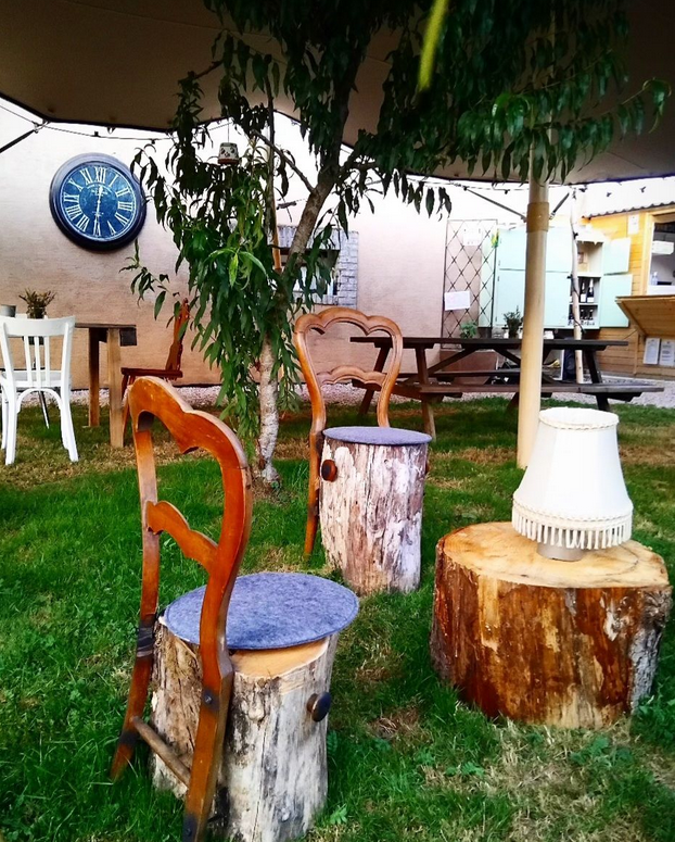 Chaises en bois posées sur des troncs d'arbres, lampes et mobilier de jardin en arrière-plan dans un espace extérieur avec un arbre et une horloge