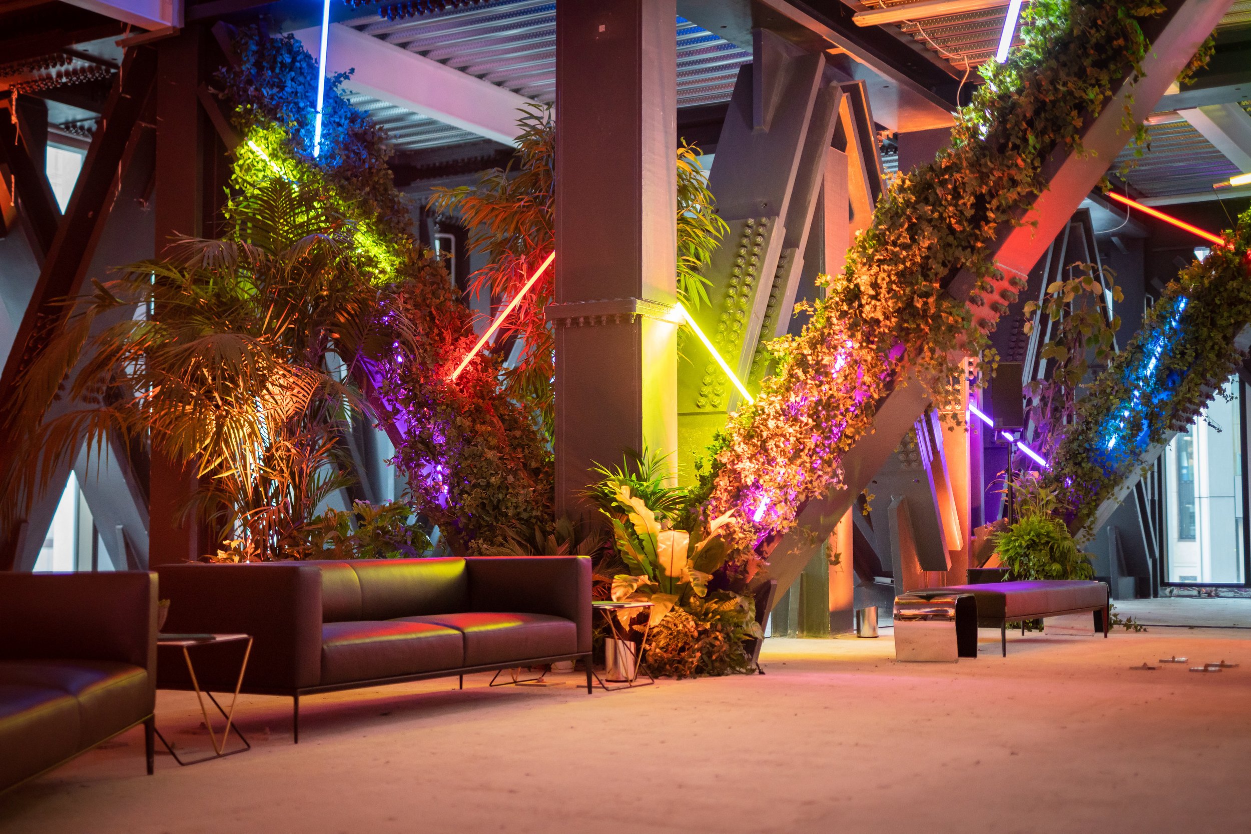 Interior of a modern building with colorful neon lights, green plants, and black couches.