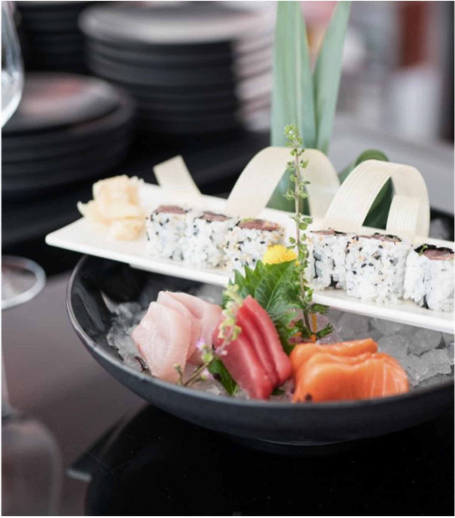 Sushi platter with assorted sashimi slices and sushi rolls decorated with green leaves and flowers, served on a bed of ice.