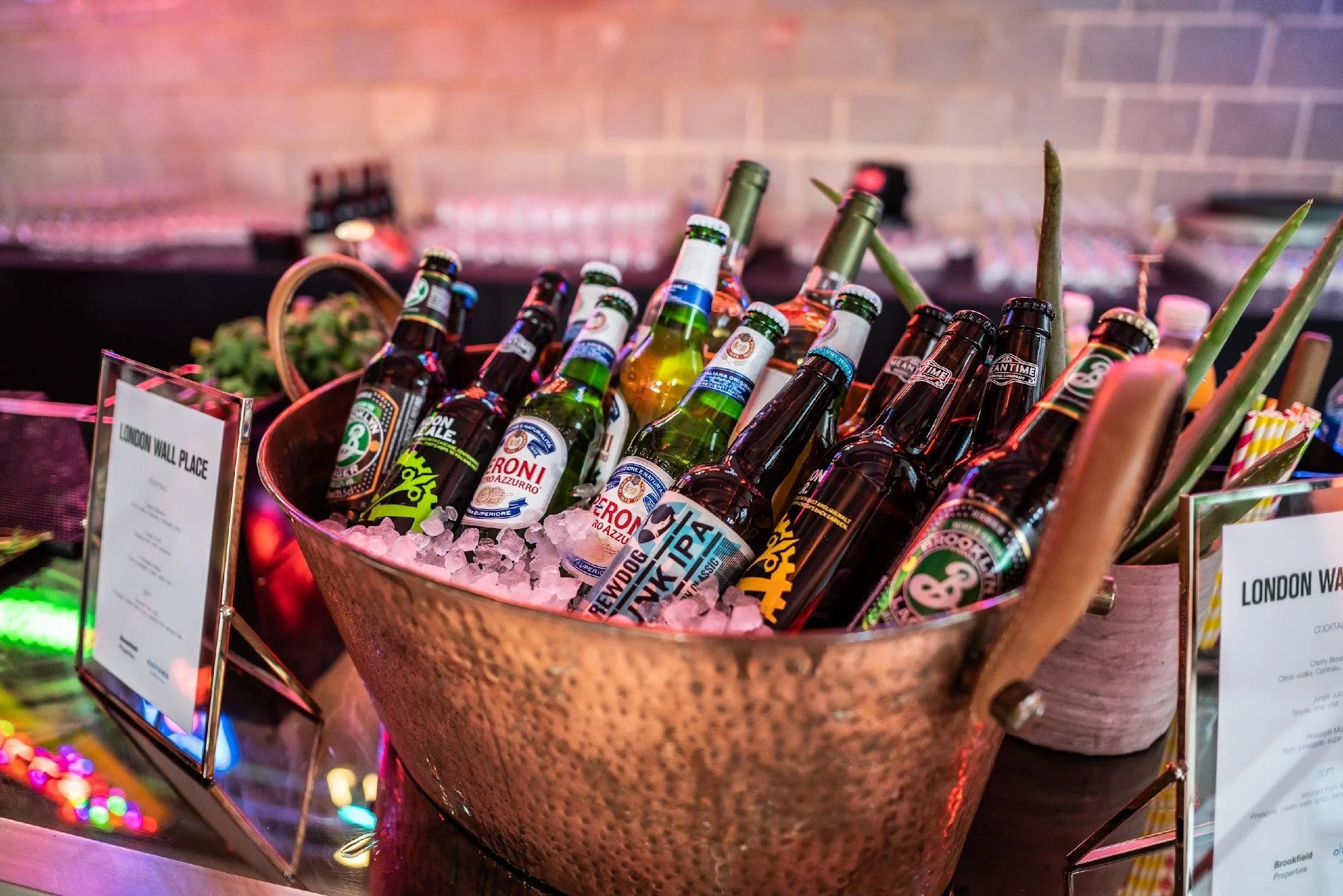 A copper bowl filled with ice and various bottles of beer at a bar or party setting.