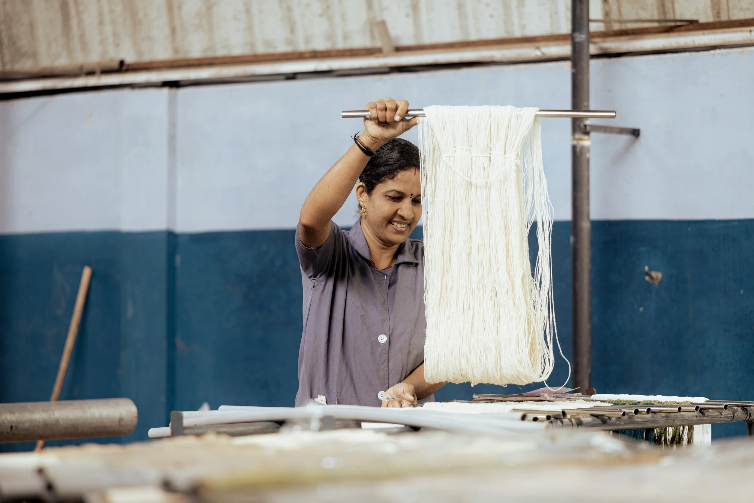 A woman hanging freshly made noodles on a horizontal rod to dry.