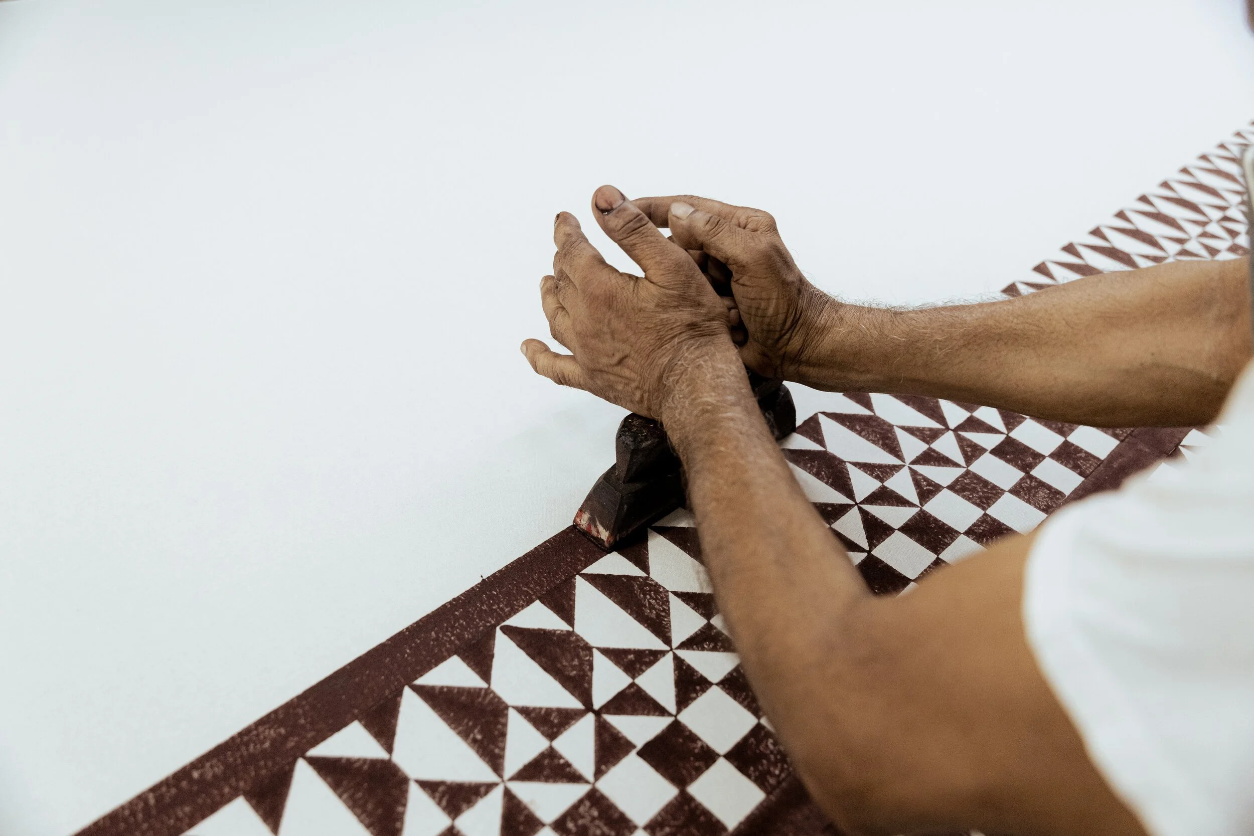 Close-up of hands shaping a piece of clay on a patterned mat, with a raised white surface in the background.