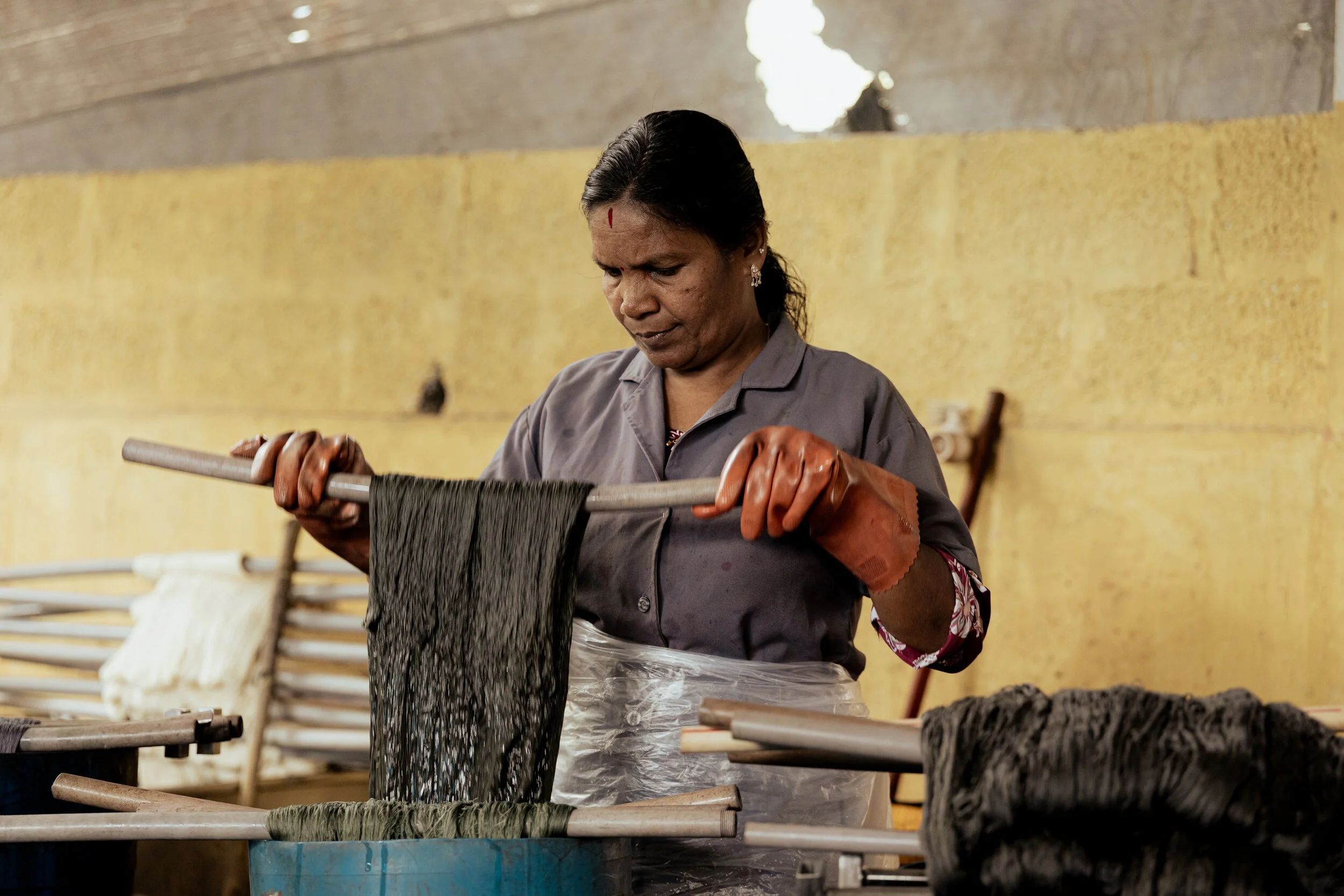 Woman working with black yarn on a wooden frame in a workshop.