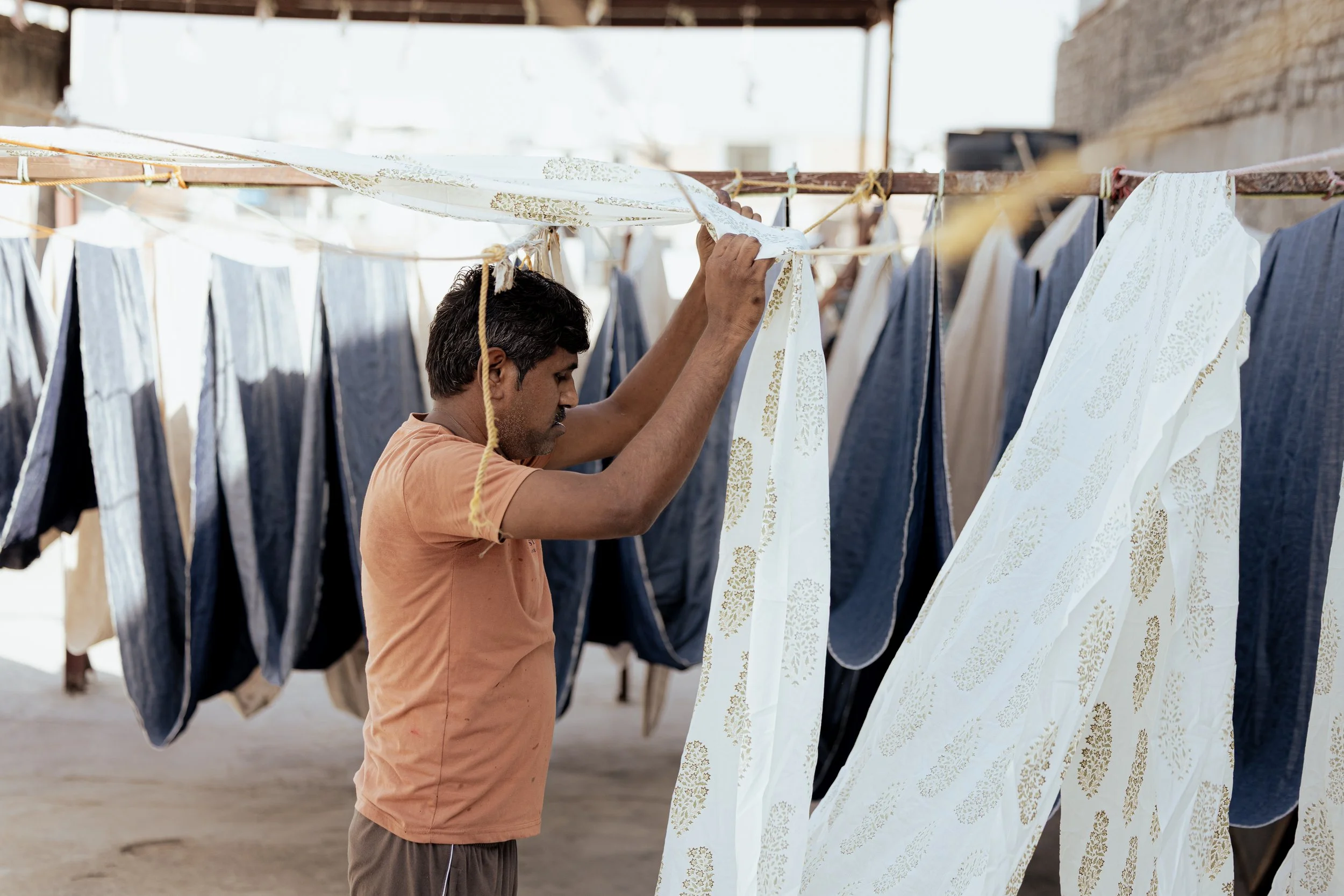 A man hanging and inspecting patterned fabric hanging on a clothesline outdoors.