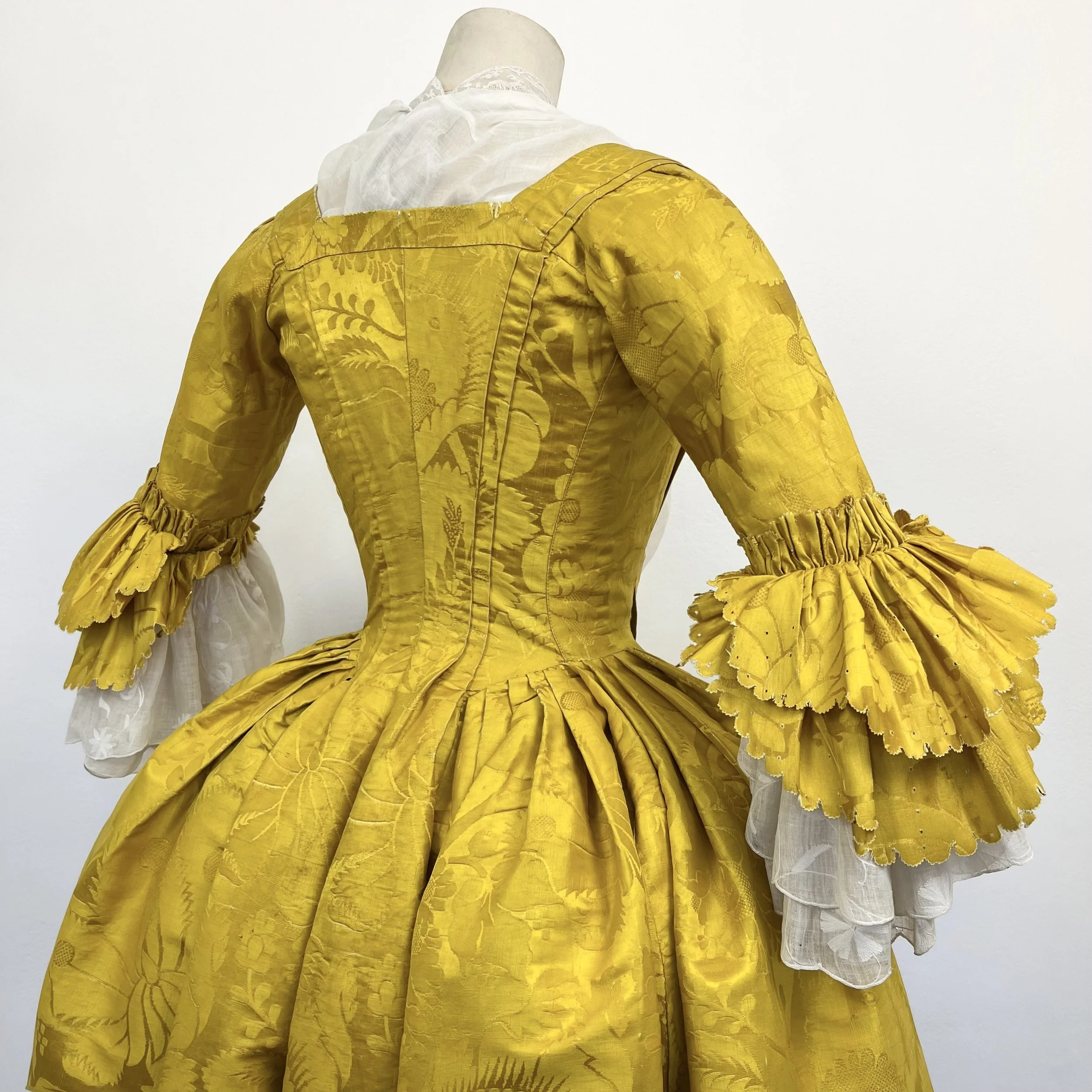 Yellow Victorian-style dress with puffed sleeves accents, displayed on a mannequin against a plain white background.