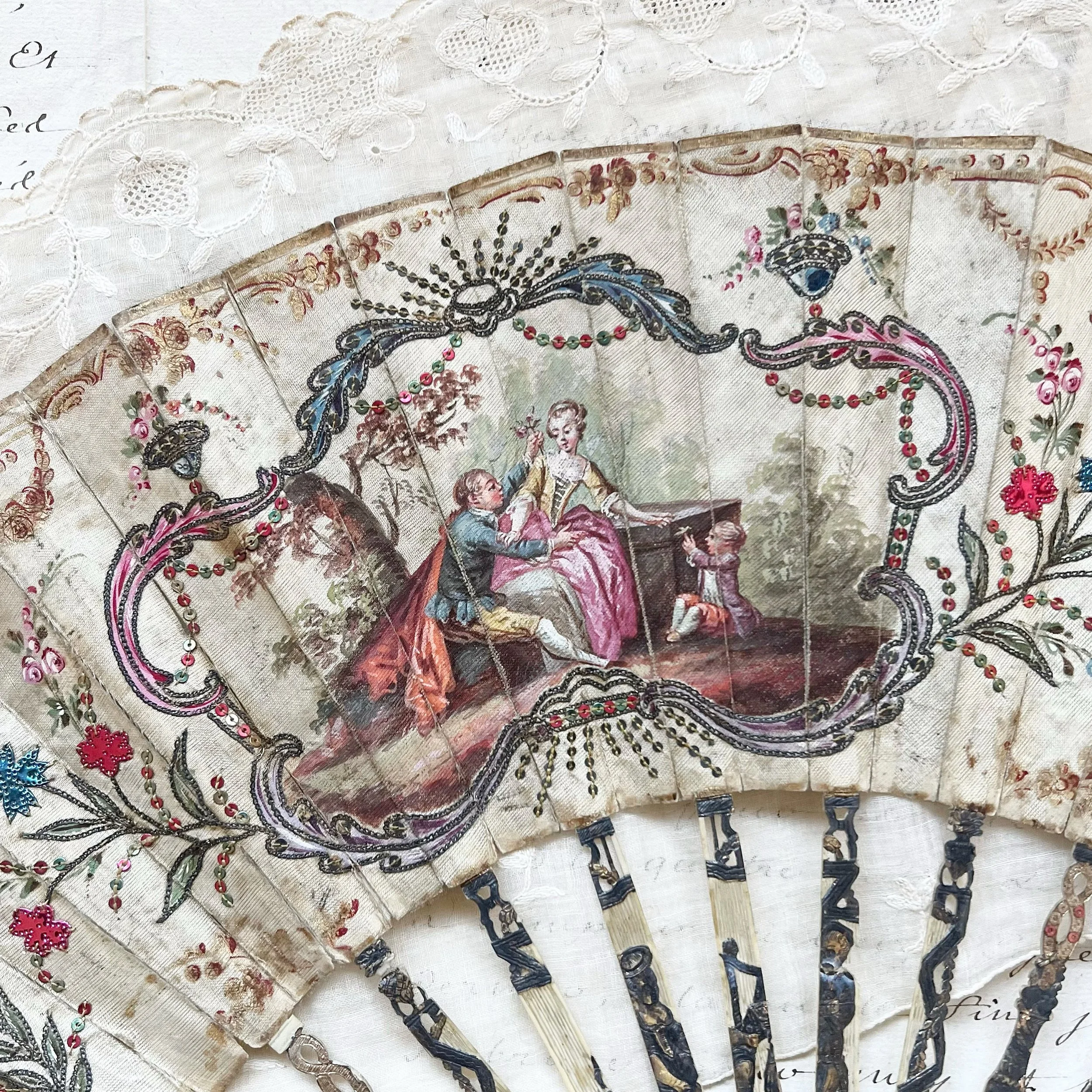 An ornate hand-painted folk art folding fan with a scene of a woman and two children, decorated with embroidered floral patterns and beads.