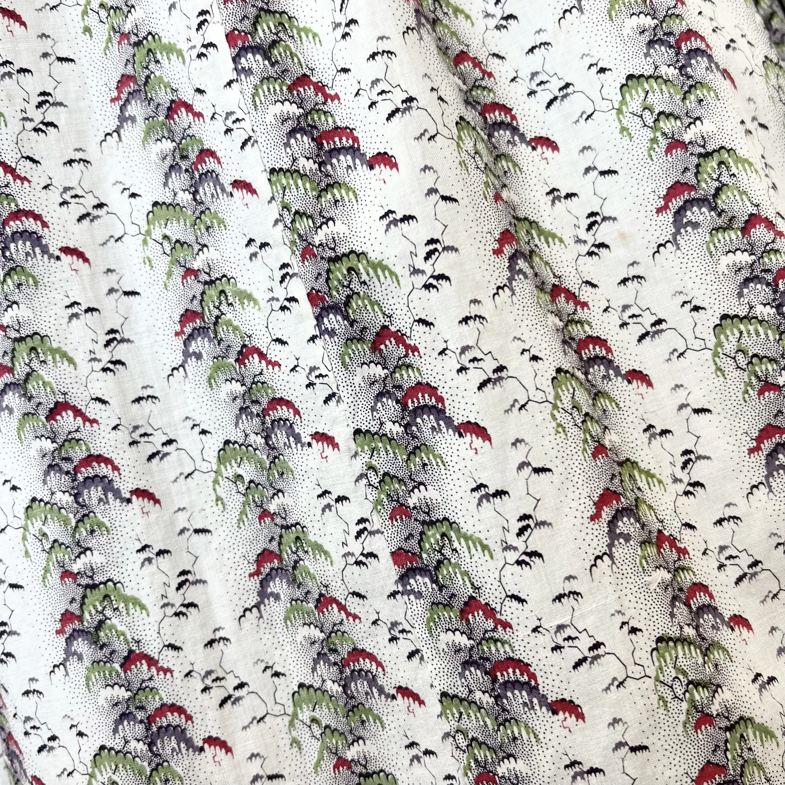 Close-up of patterned fabric with red, green, black, and gray designs on a white background, resembling stylized trees or mountains.