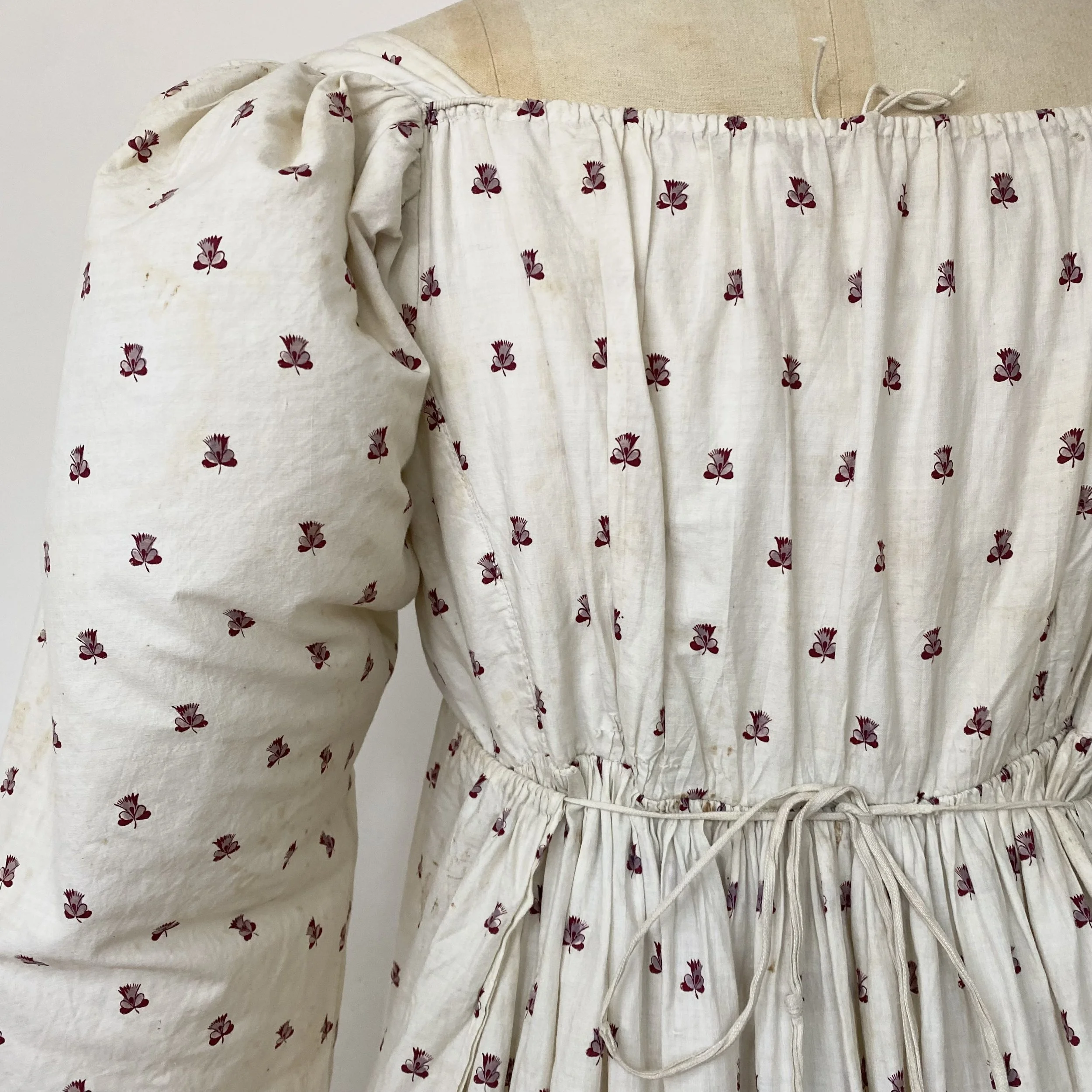 Close-up of a fabric with a cream background and small red floral patterns, gathered with a drawstring.