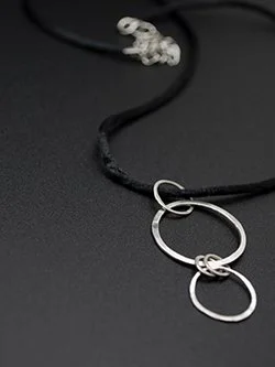 Handcrafted sterling silver interlocking double circle pendant on a black satin cord necklace with two graduated hammered silver hoops, handmade by Jennifer Morris