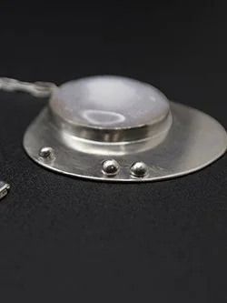 Handcrafted sterling silver pendant necklace with a luminous translucent moonstone cabochon on a brushed silver disc base with decorative ball accents on a silver chain, by Jennifer Morris