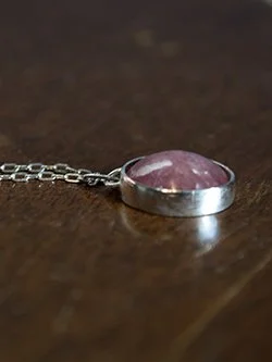 Handcrafted sterling silver pendant necklace with a pink rhodochrosite cabochon in a smooth bezel setting on a delicate silver chain, handmade by Jennifer Morris
