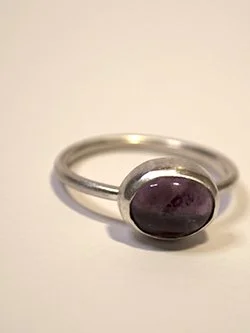 Handcrafted sterling silver ring with a deep purple oval amethyst cabochon in a smooth bezel setting on a minimalist thin band, by Jennifer Morris