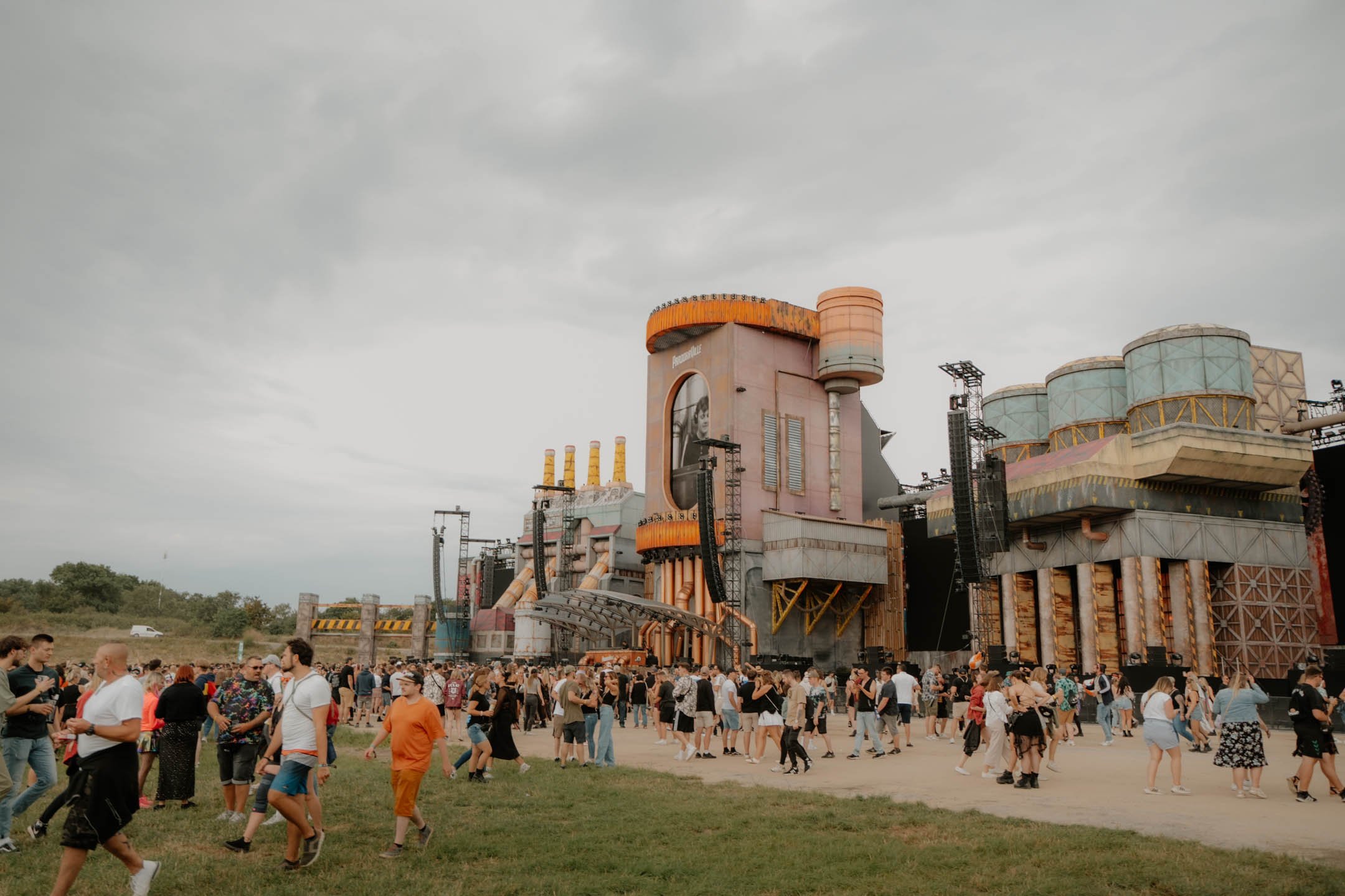Menschenmenge vor einem großen, futuristisch aussehenden Bauwerk bei einem Festival oder Konzert, das mit Lautsprechern und Bühnen ausgestattet ist.