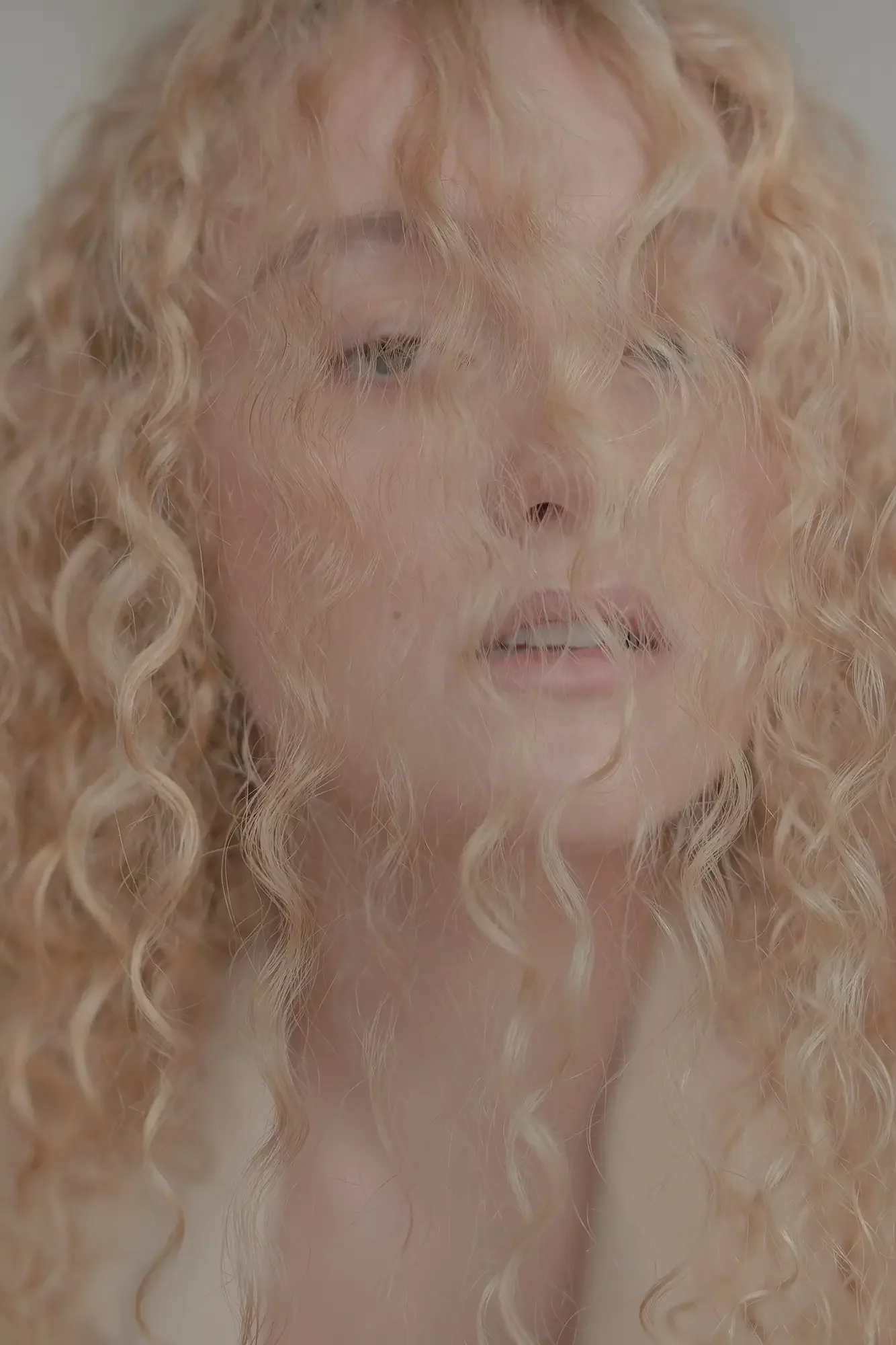 Close-up of a woman with long, blonde, curly hair partially covering her face, with some strands over one eye.