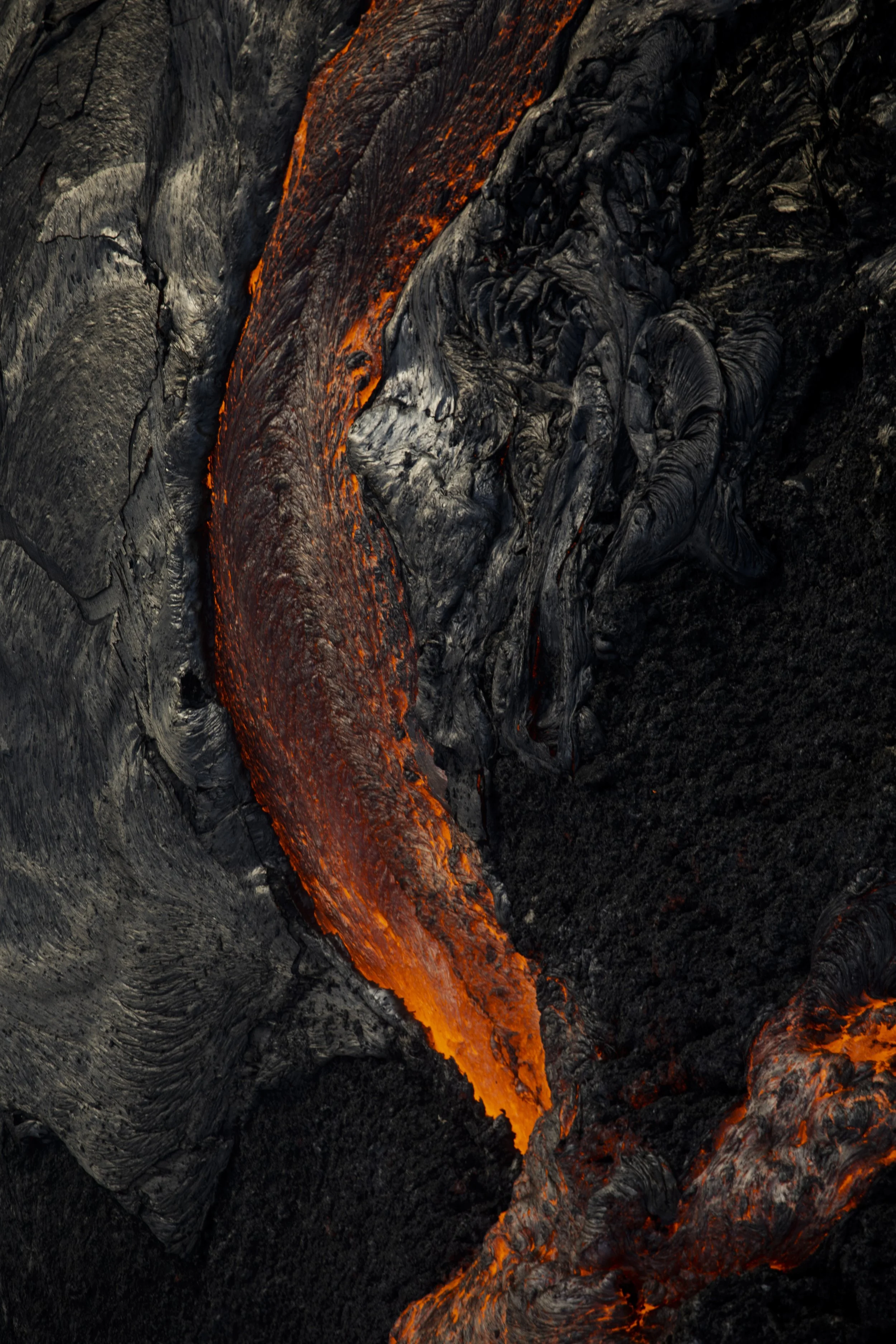 Close-up photo of flowing lava oozing over dark volcanic rocks.