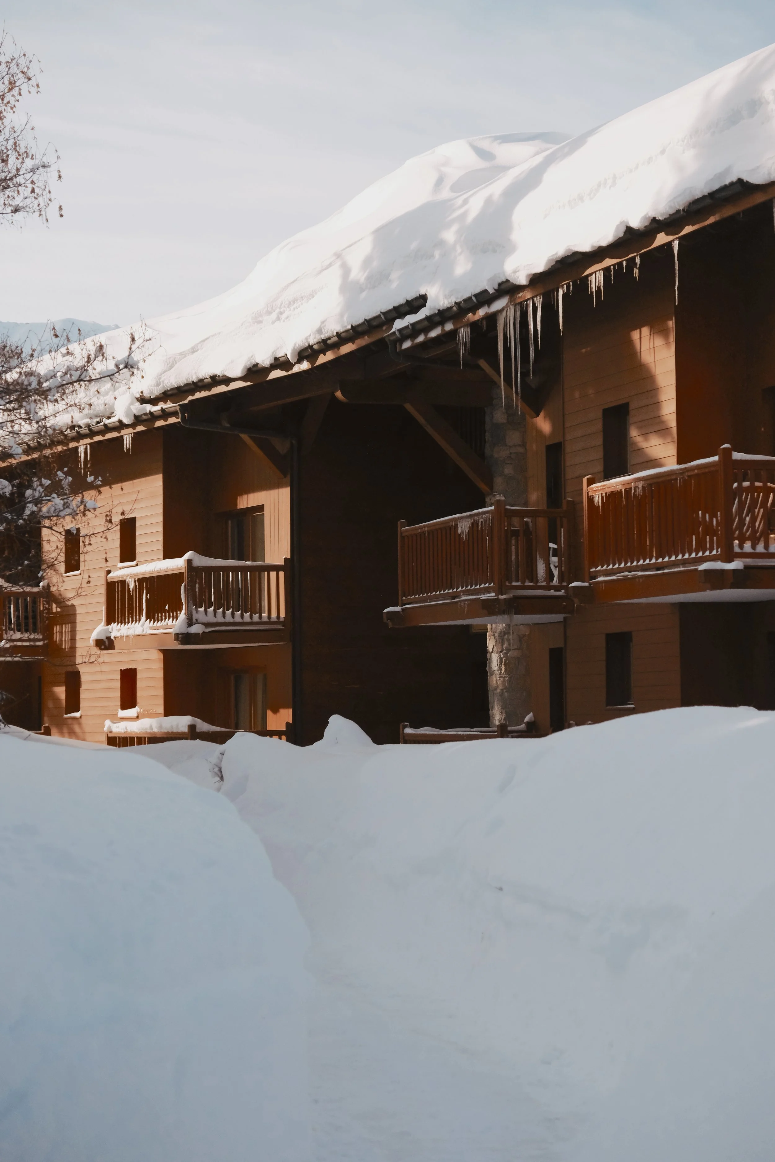 Snow-covered wooden house with icicles hanging from the roof, surrounded by a thick layer of snow.
