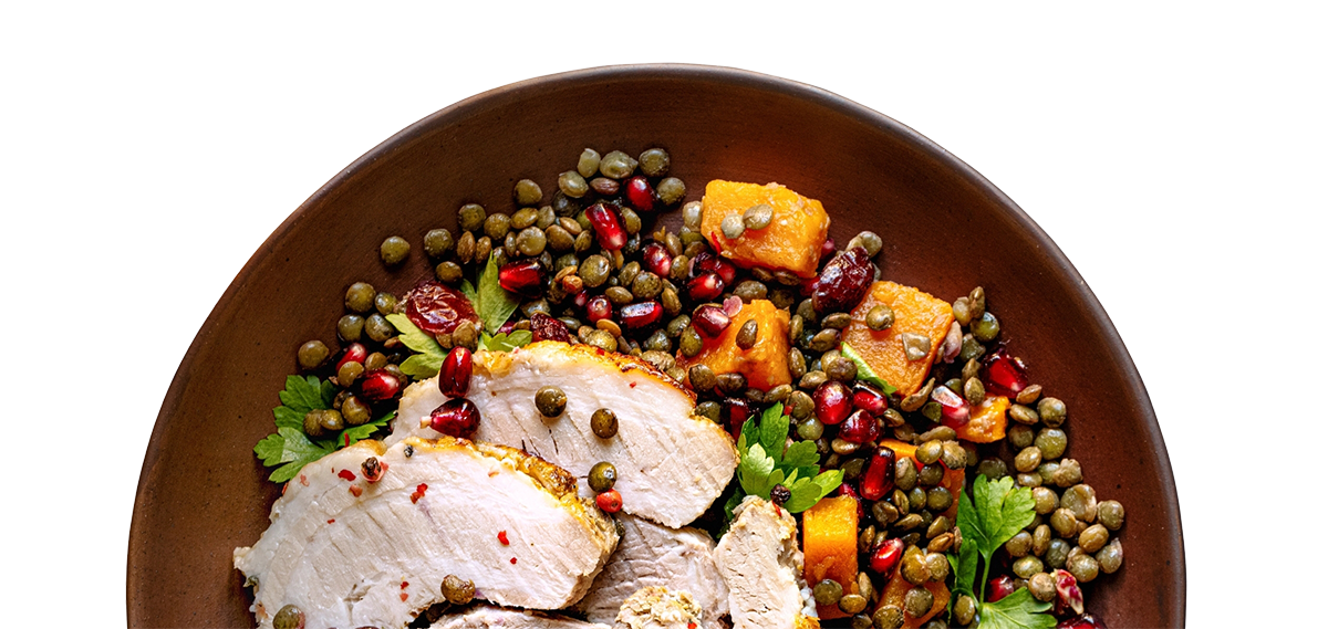A bowl of cooked chicken breast served with vegetables, lentils, pomegranate seeds, and fresh parsley.