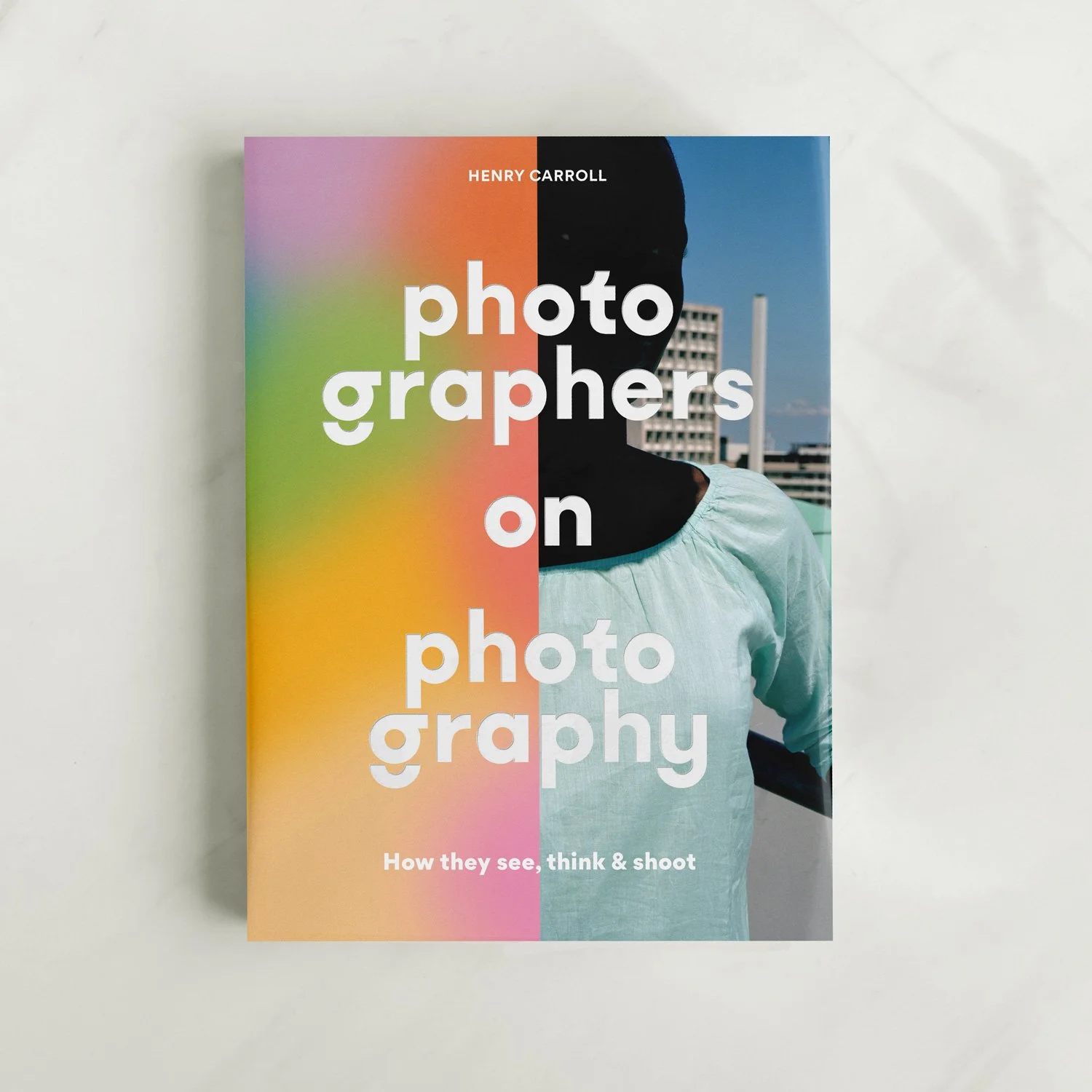 Book titled 'Photographers on Photography' by Henry Carroll, featuring a person with a dark silhouette against an urban background, with a colorful rainbow gradient on the left side of the cover.