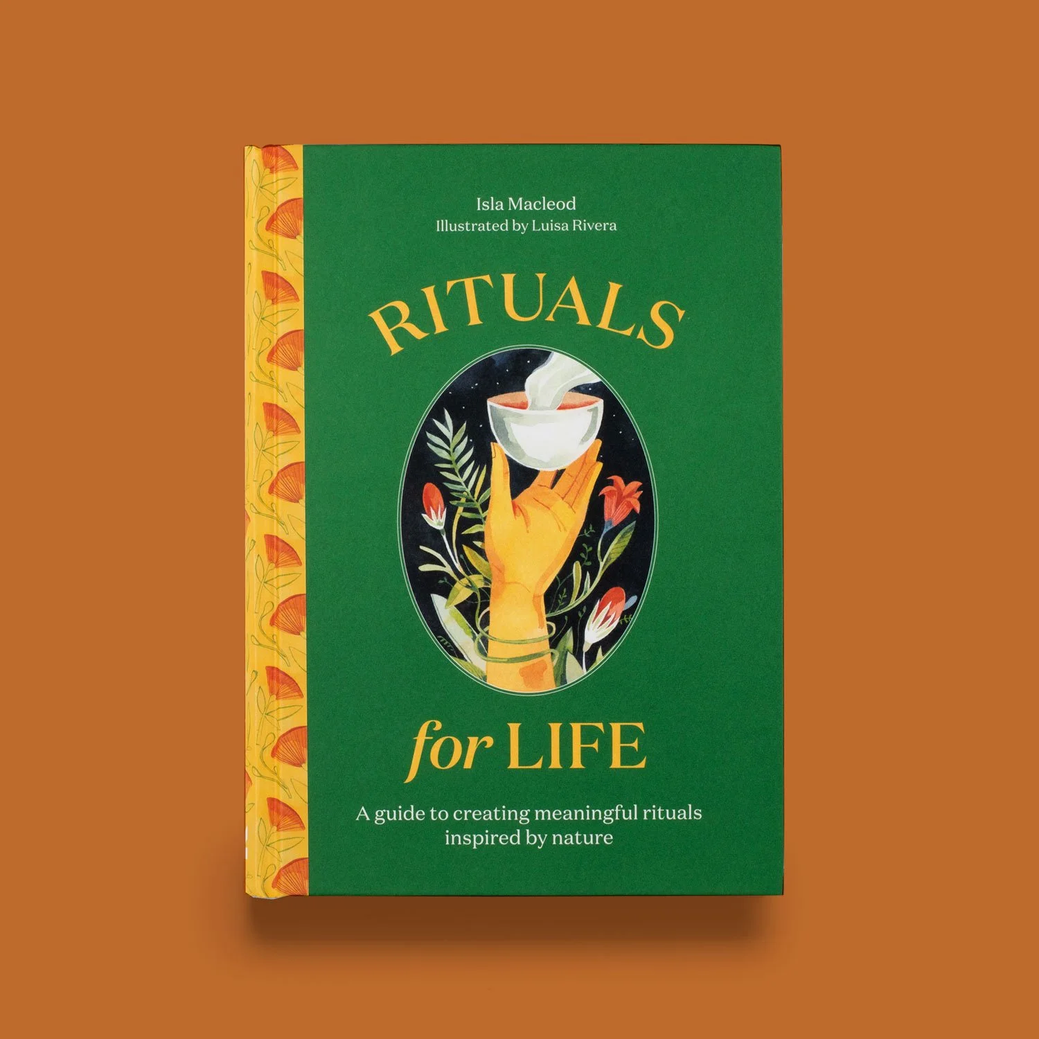 A book titled "Rituals for Life" with a green cover and a colorful illustration of a hand holding a steaming bowl, surrounded by floral patterns on the spine and a warm brown background.